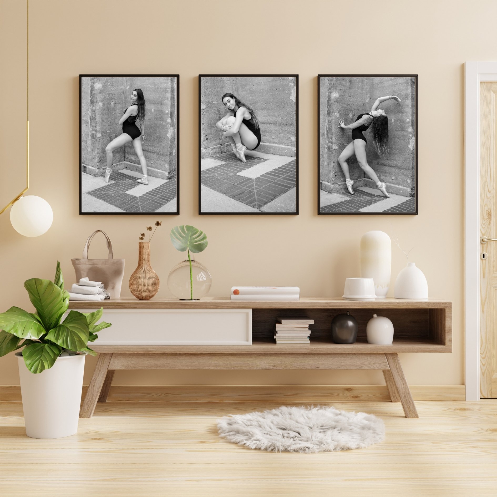 Modern living room interior with three black and white framed ballet dancer photos on the wall, a wooden shelf with decorative items, a potted plant, and a hanging lamp.