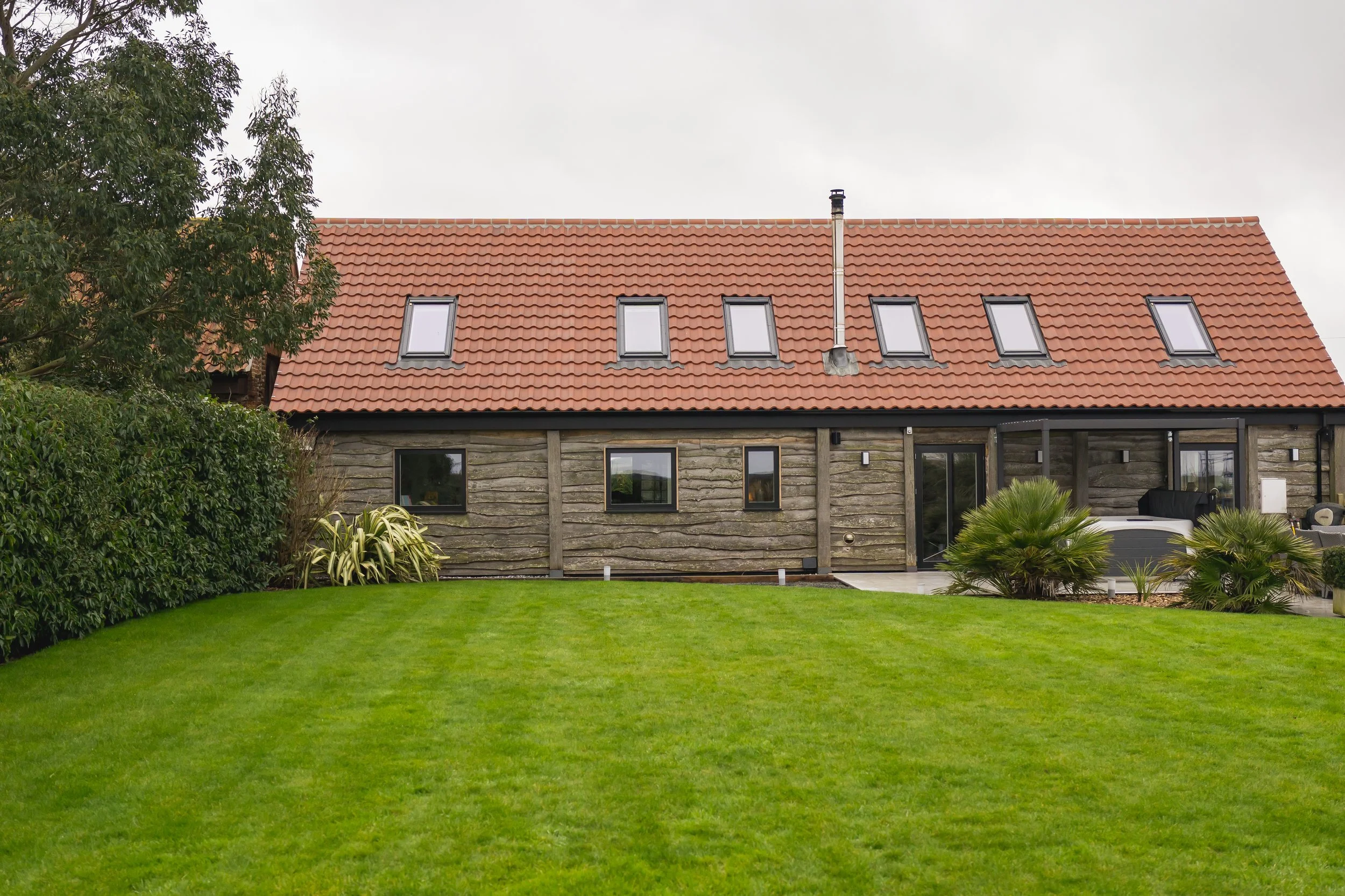 A beautiful rural but modern barn conversion with an outdoor hot tub, green lawn and enclosed garden on a spring day in the North Norfolk Coast