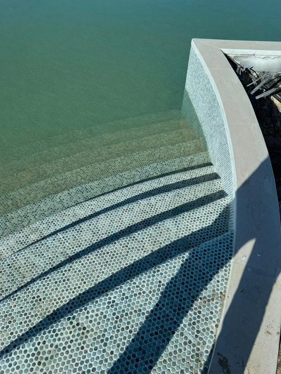 Water feature with steps leading into a pool, surrounded by a curved edge and mosaic tiles.