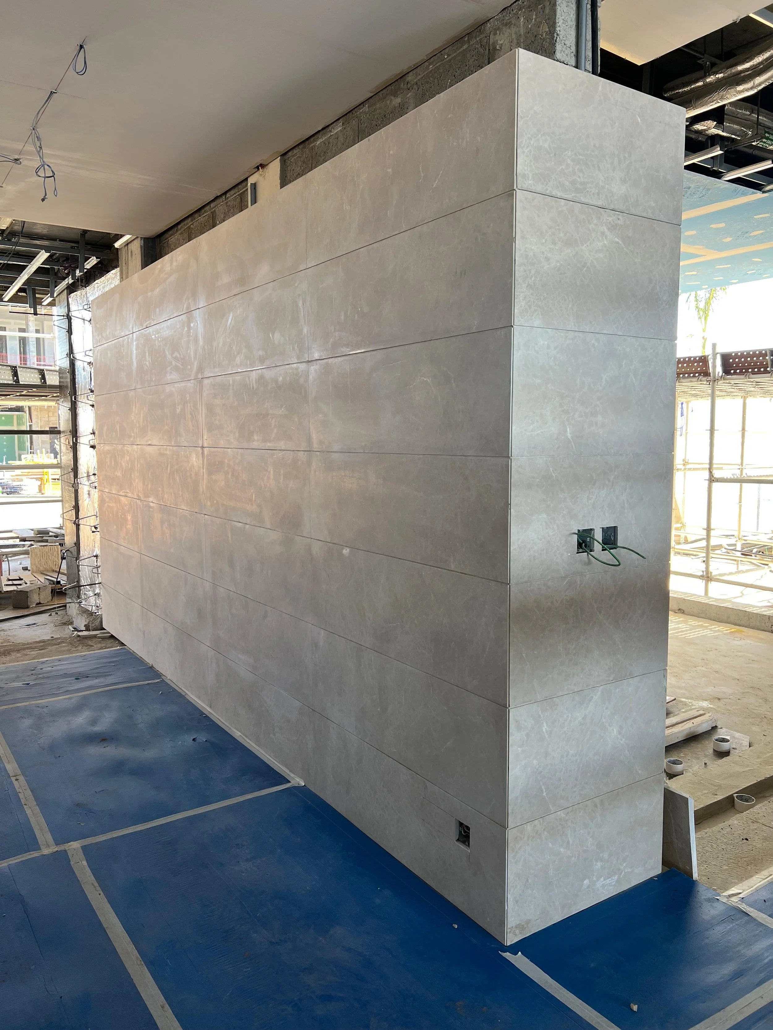 Interior view of an unfinished building with a large tiled wall, electrical outlets on the side, and construction materials on the floor.