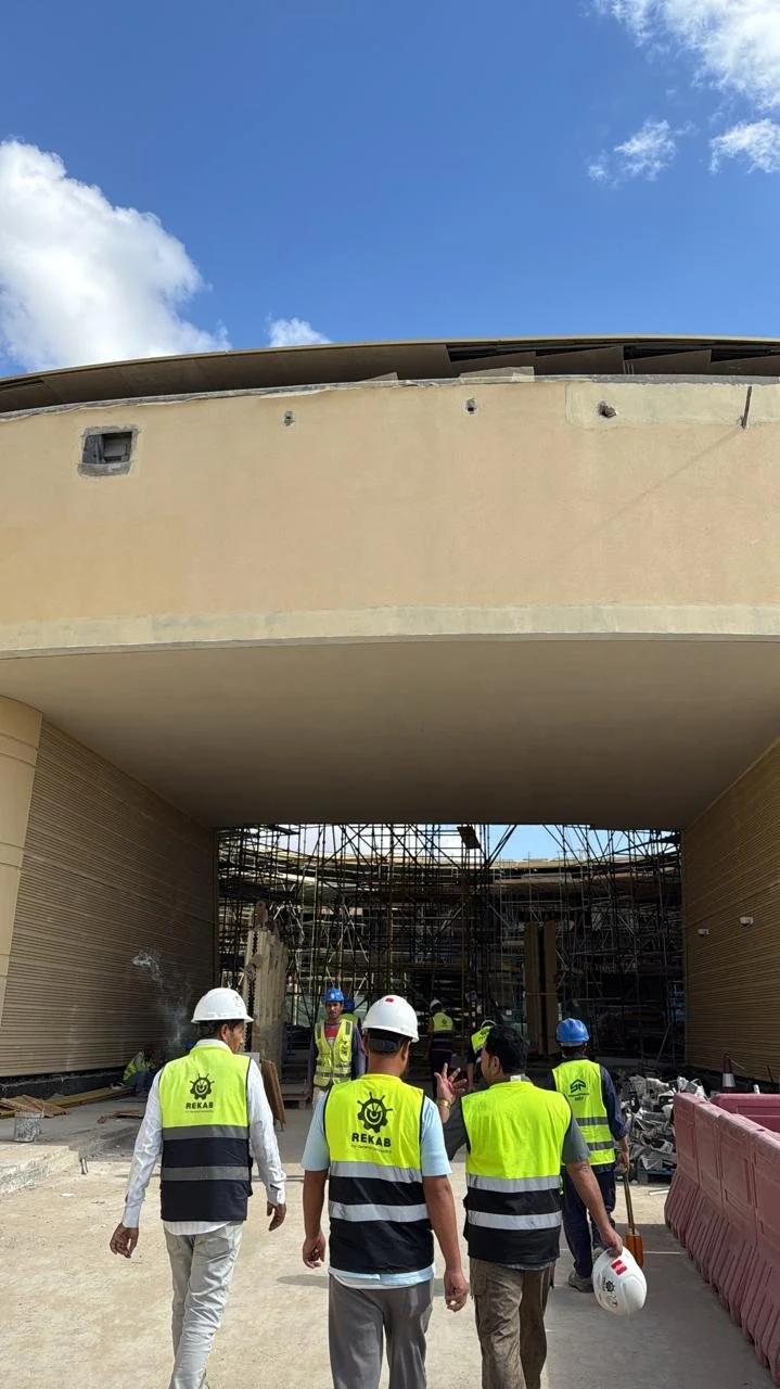 Modern building under construction against a clear blue sky, featuring scaffolding and architectural columns.