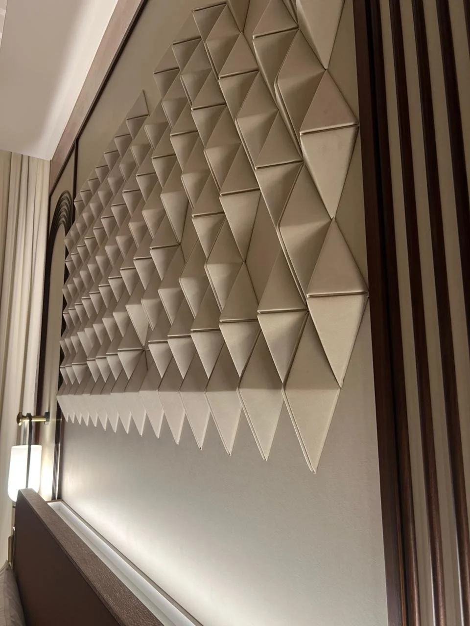 A geometric wall decoration composed of interconnected beige fabric-covered triangular modules arranged in a grid pattern.