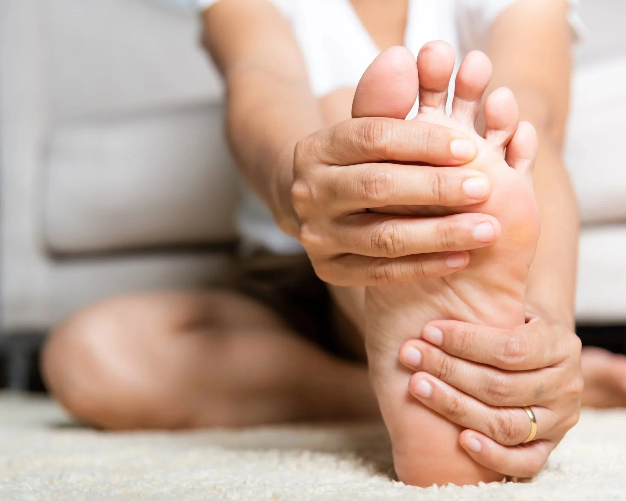 A person holding their ankle, indicating pain or discomfort in their foot.
