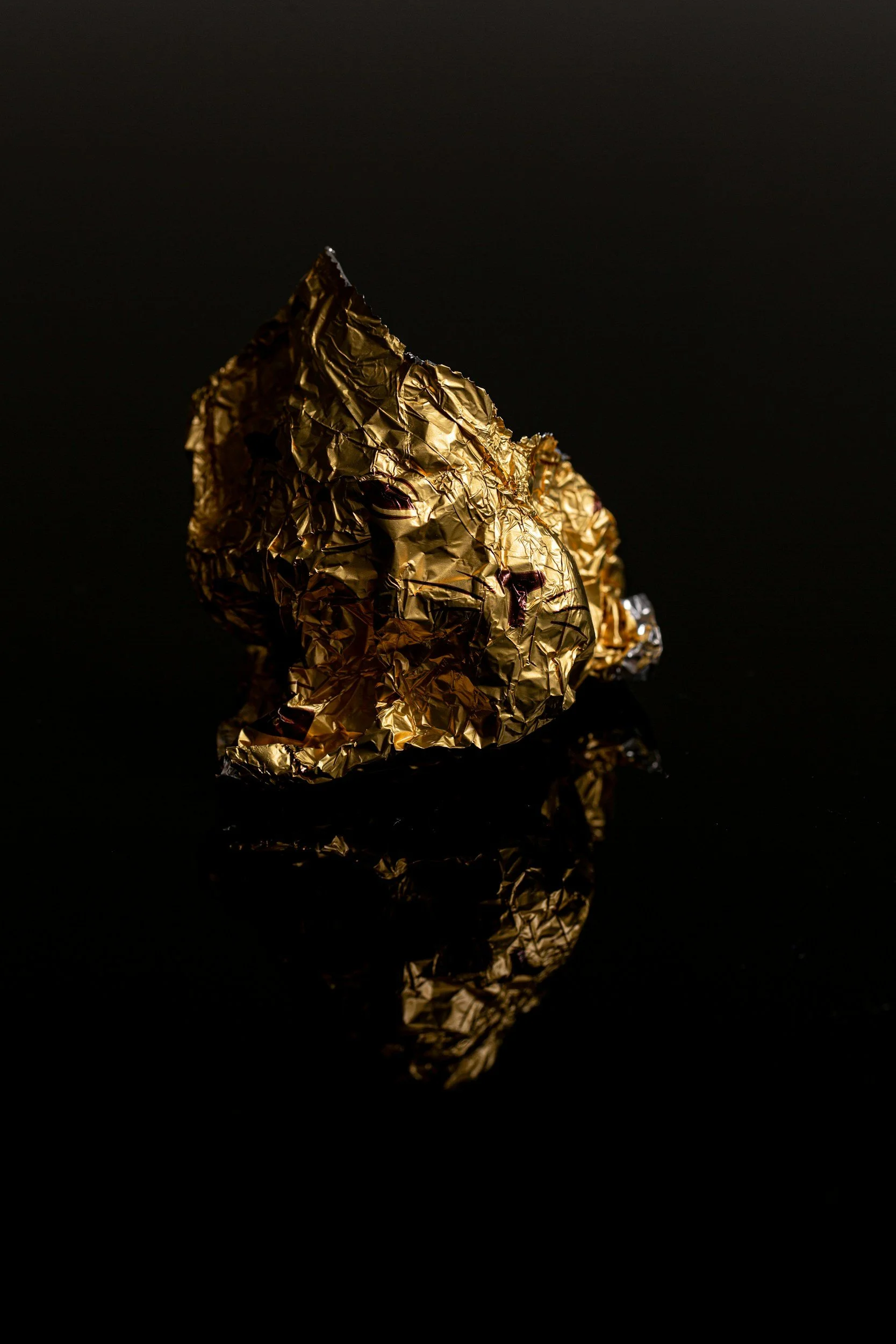 A crumpled piece of gold foil with a reflection on a dark surface.