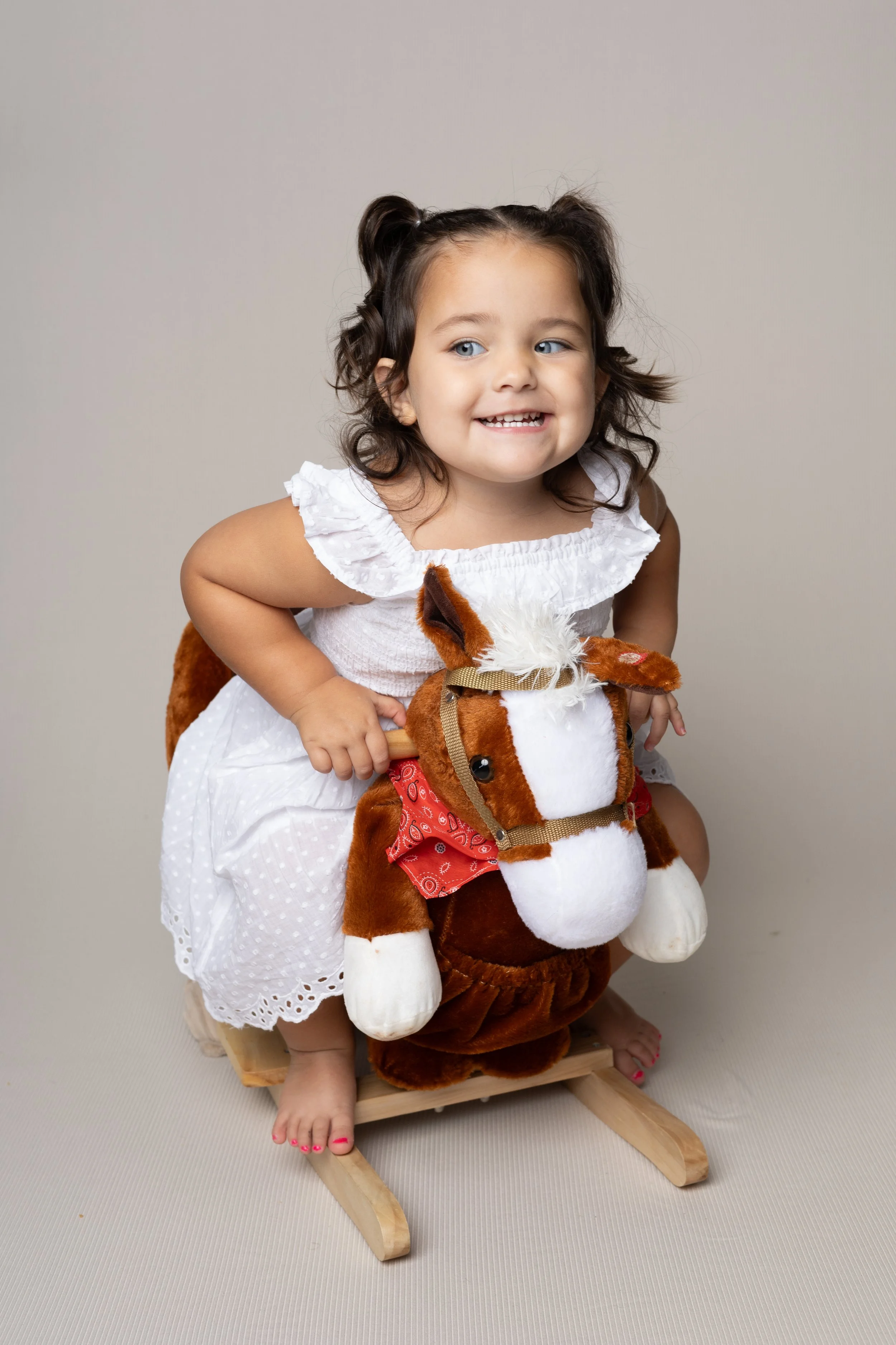A young girl with brown hair in pigtails riding a toy rocking horse.