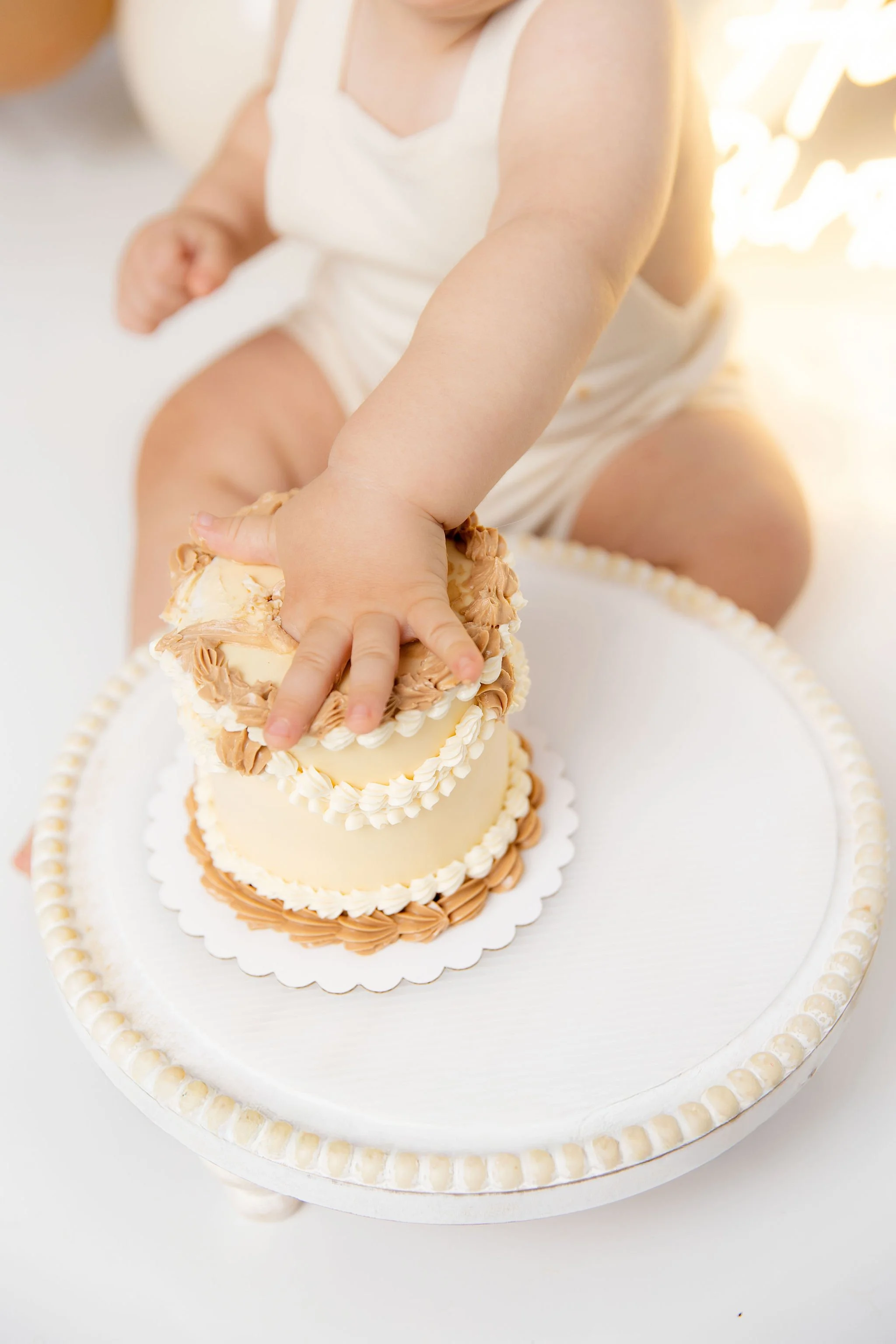 Child reaching for a small, decorated birthday cake on a white tray.