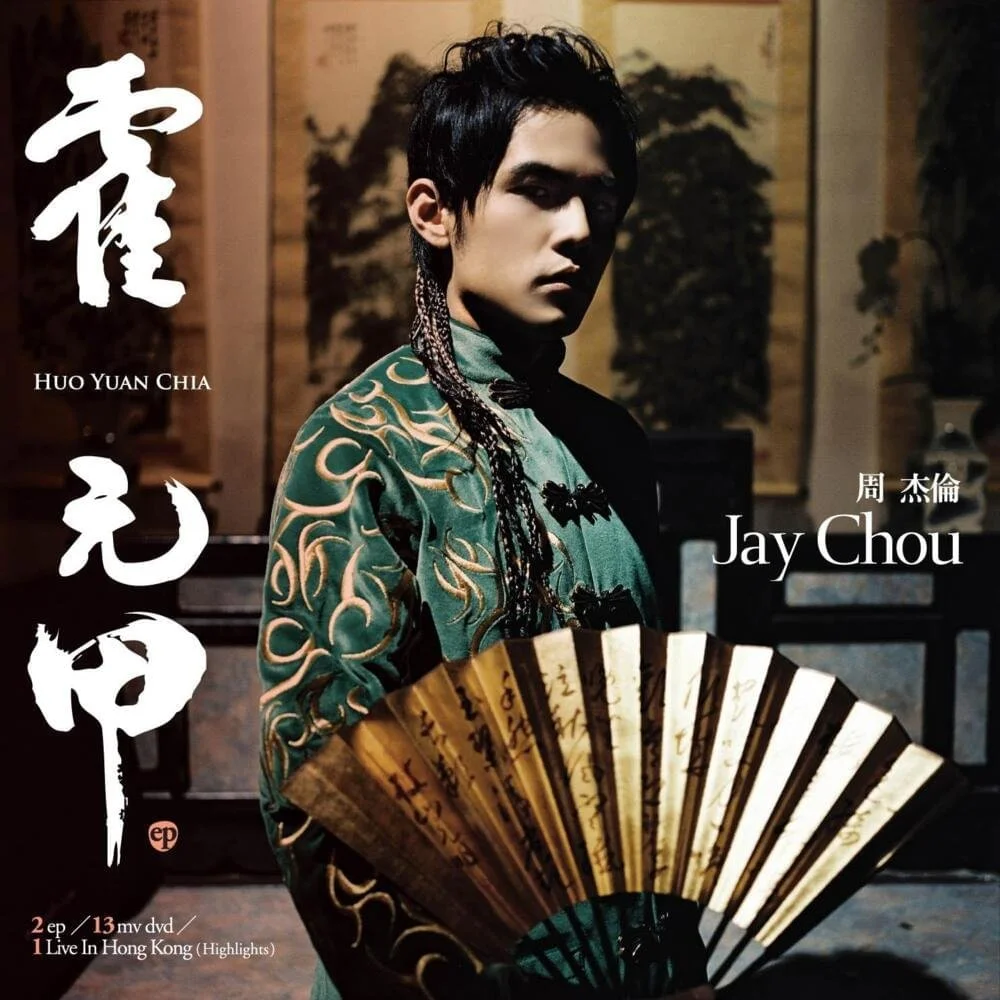 A young man dressed in traditional Asian clothing holding a folding fan, with Chinese calligraphy and text, including the names Jay Chou and Huo Yuan Chia, on a background featuring Asian artwork.