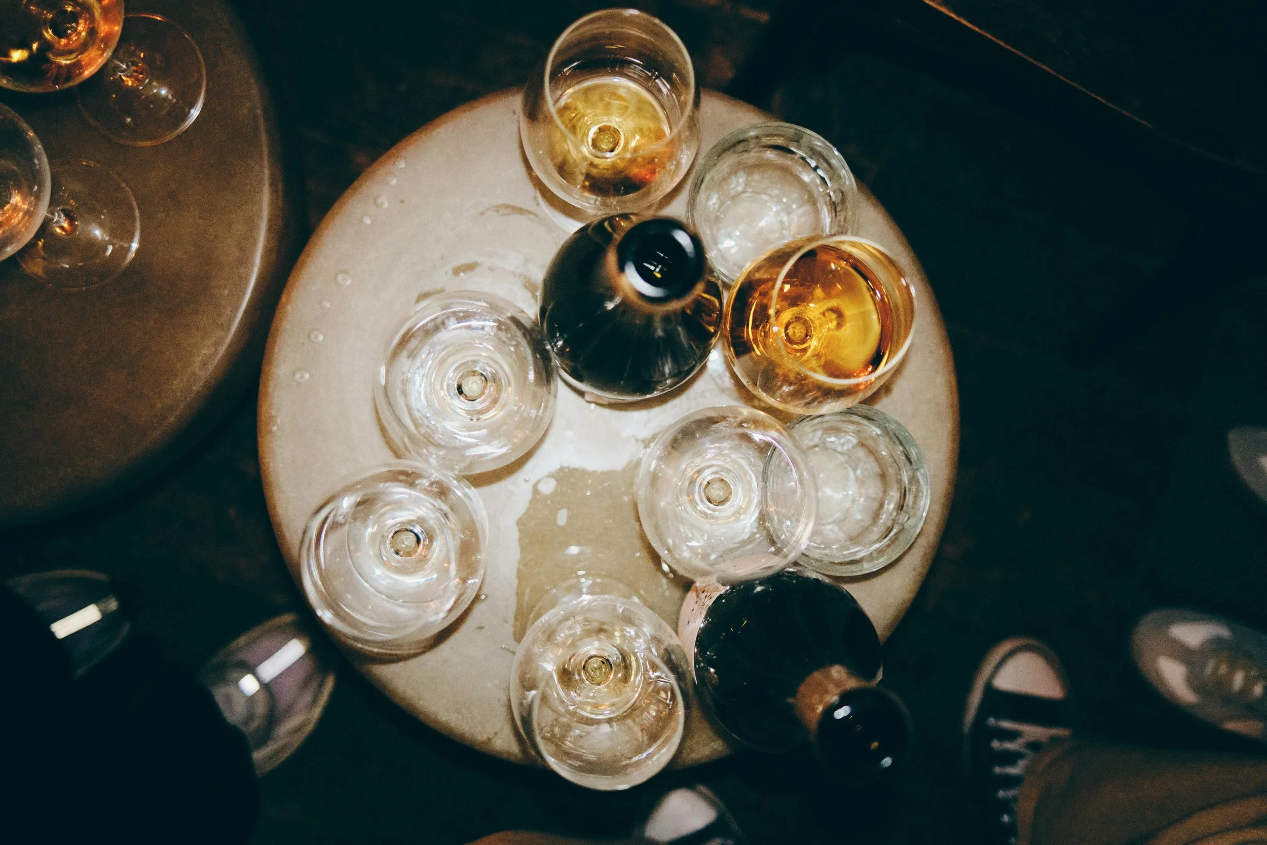Top-down view of several empty and partially filled wine glasses on a round table at a bar or restaurant.