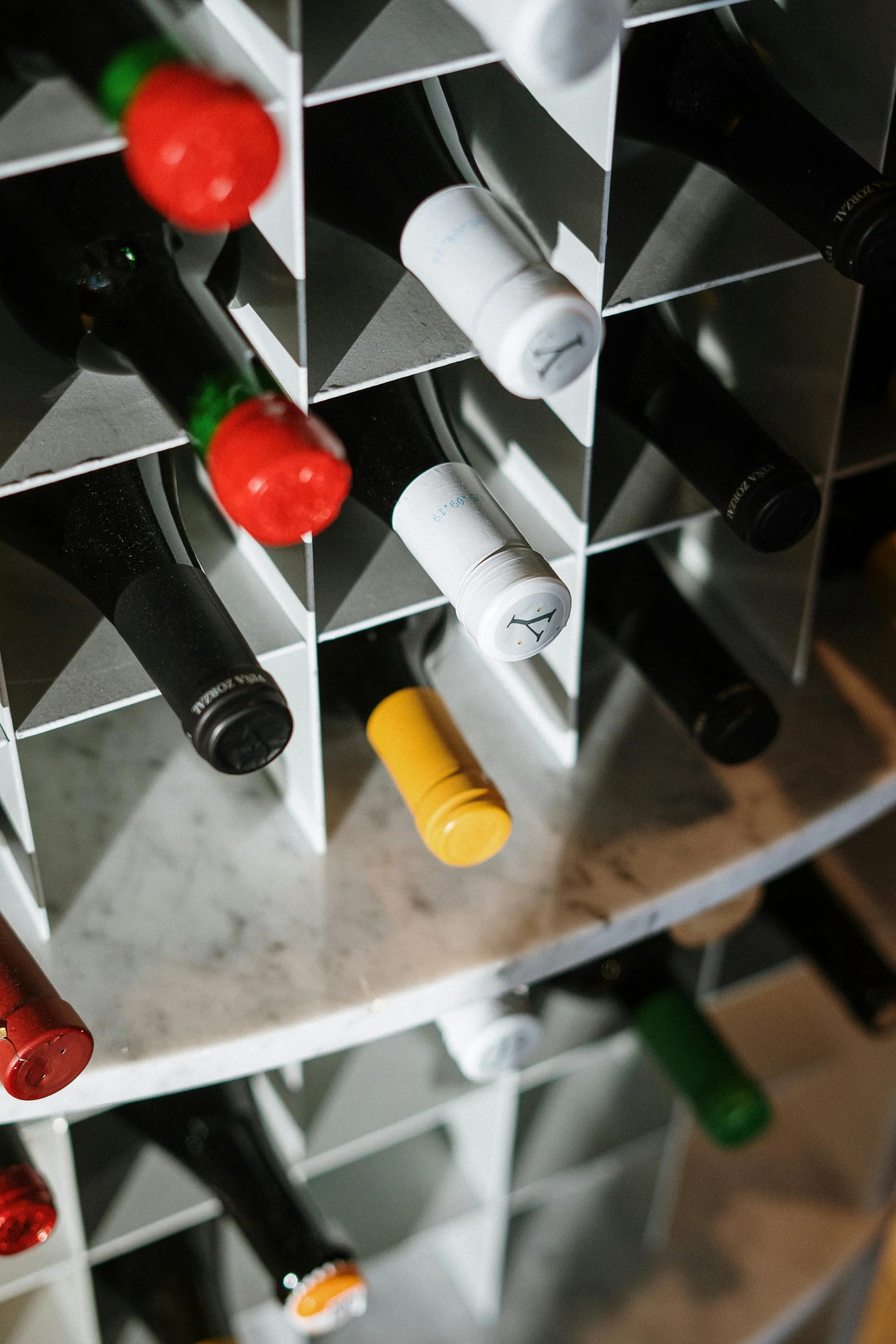 Close-up of a wine rack with bottles stored horizontally, showing various bottle caps including red, white, black, yellow, and green.