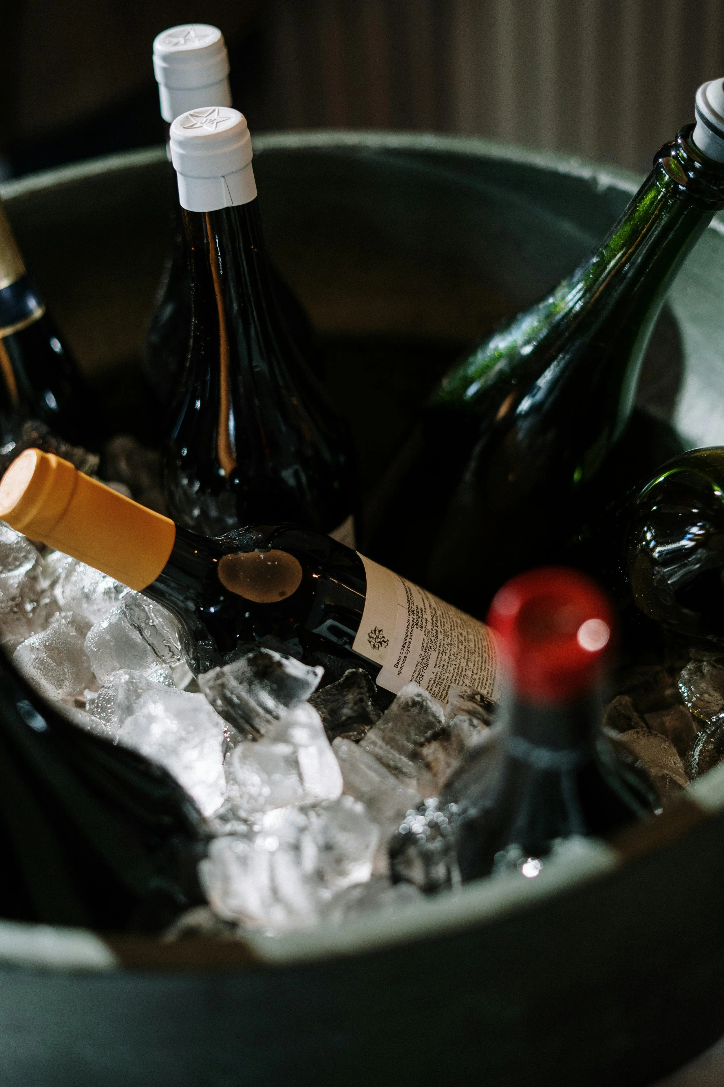 Several bottles of wine and beverages chilling in a bucket with ice.