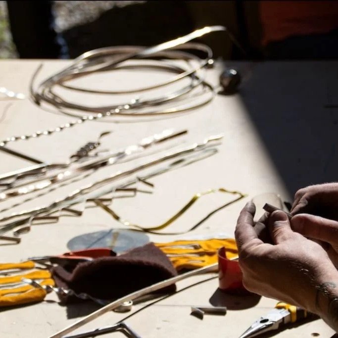 A visitor works on a metal sculpture piece at a worktable with various metal tools and wires, part of one of KOAC's many artist workshops.