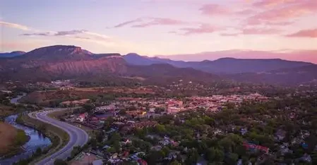 A scenic view of a town at sunset with mountains in the background and a river winding through the landscape.