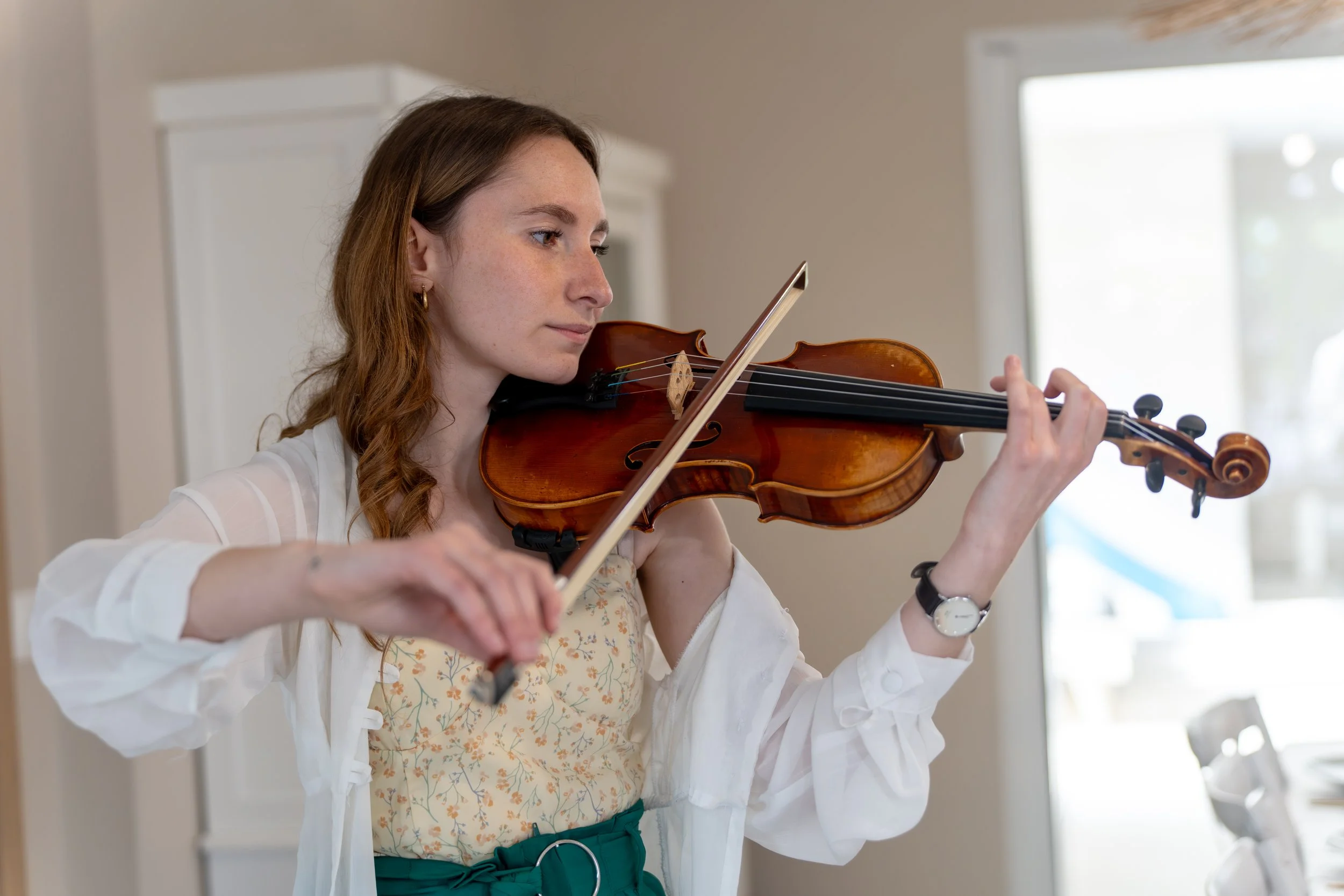 Une femme joue du violon dans une pièce lumineuse.