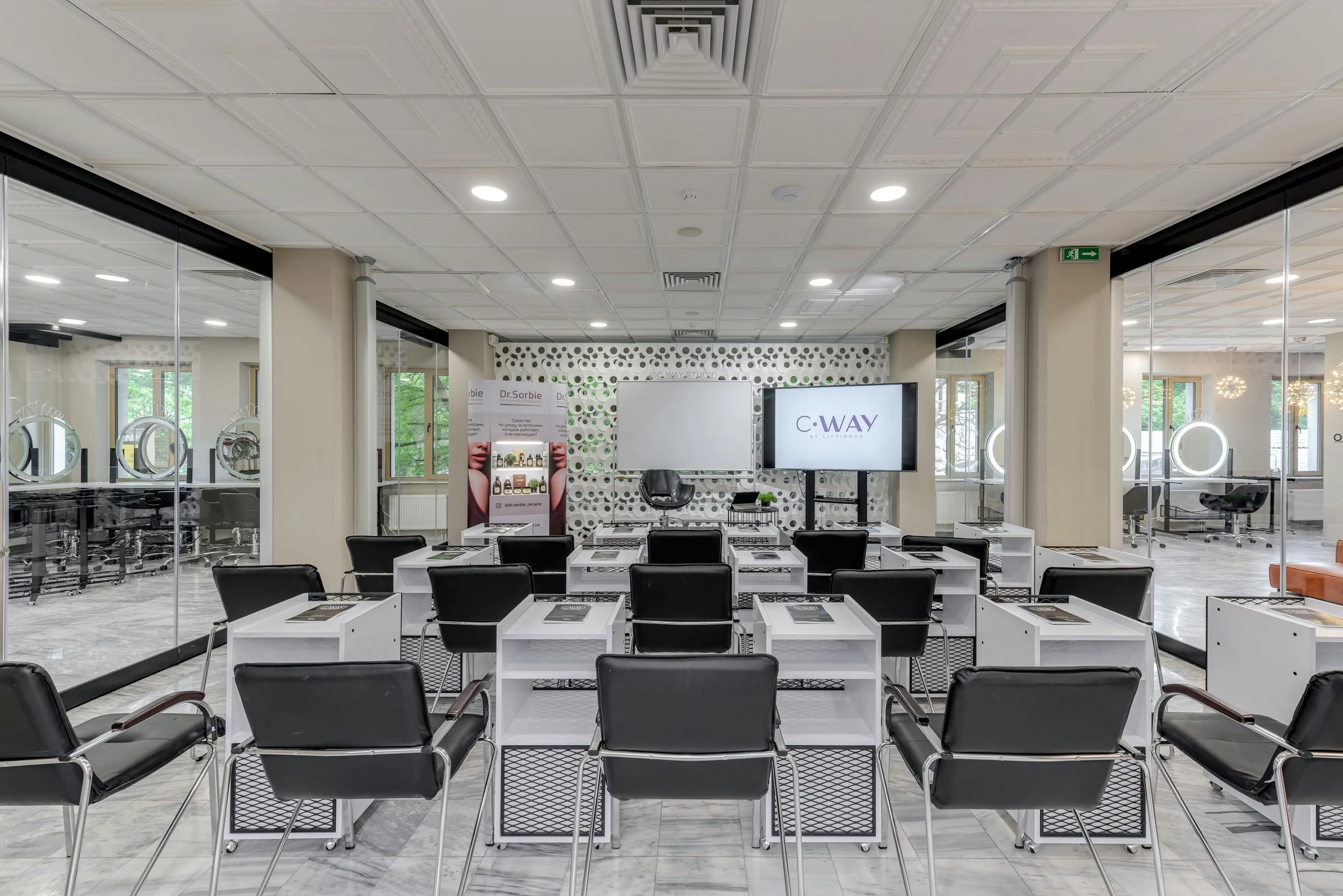 Salle de formation moderne avec bureaux et chaises noires, tableau blanc et écran affichant "C-WAY". évènements d'entreprise, conférence, séminaire, salon d'entreprise