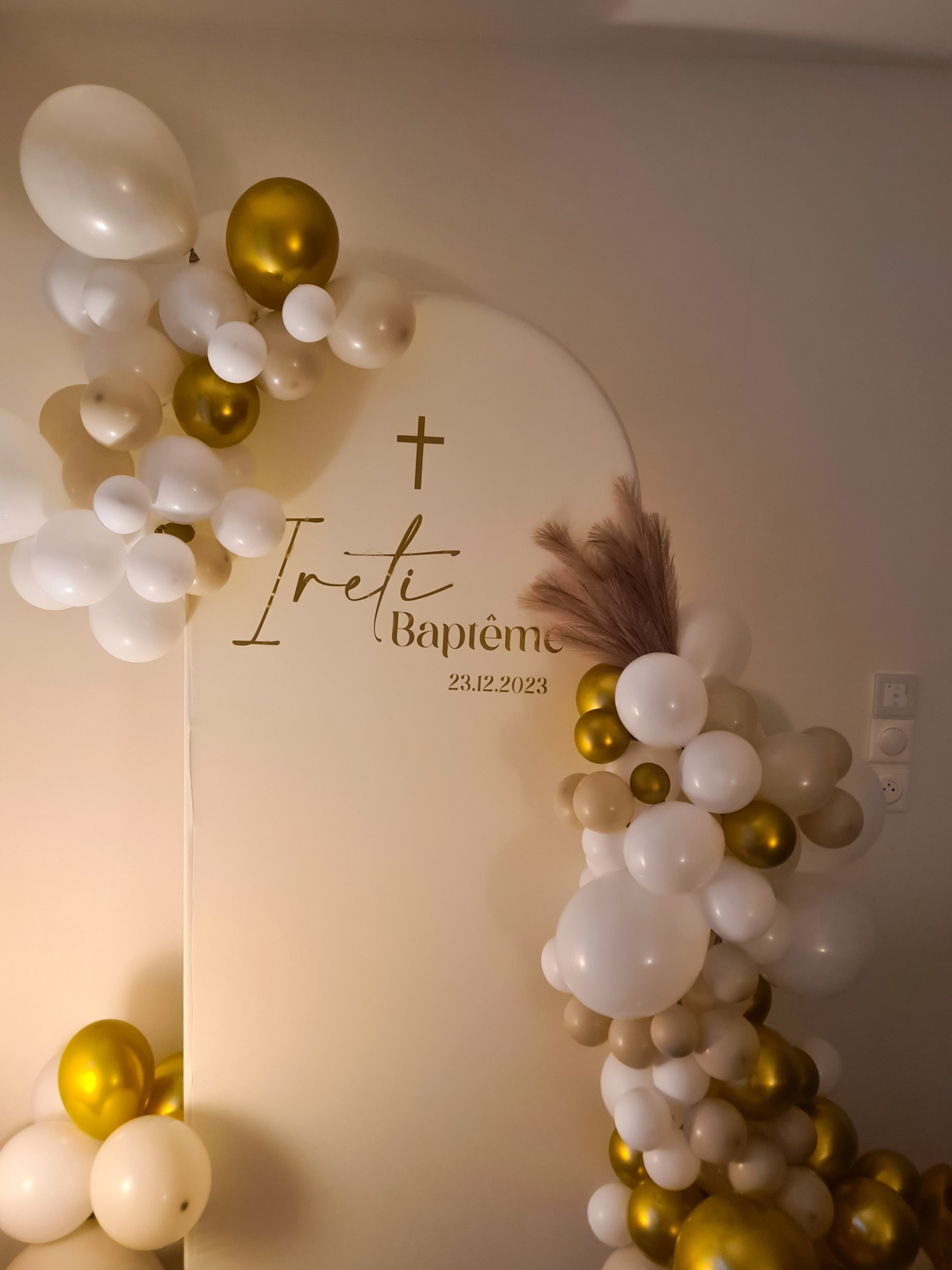 Décoration de baptême avec des ballons blancs et dorés, une croix et la date "23.12.2023" sur un panneau.