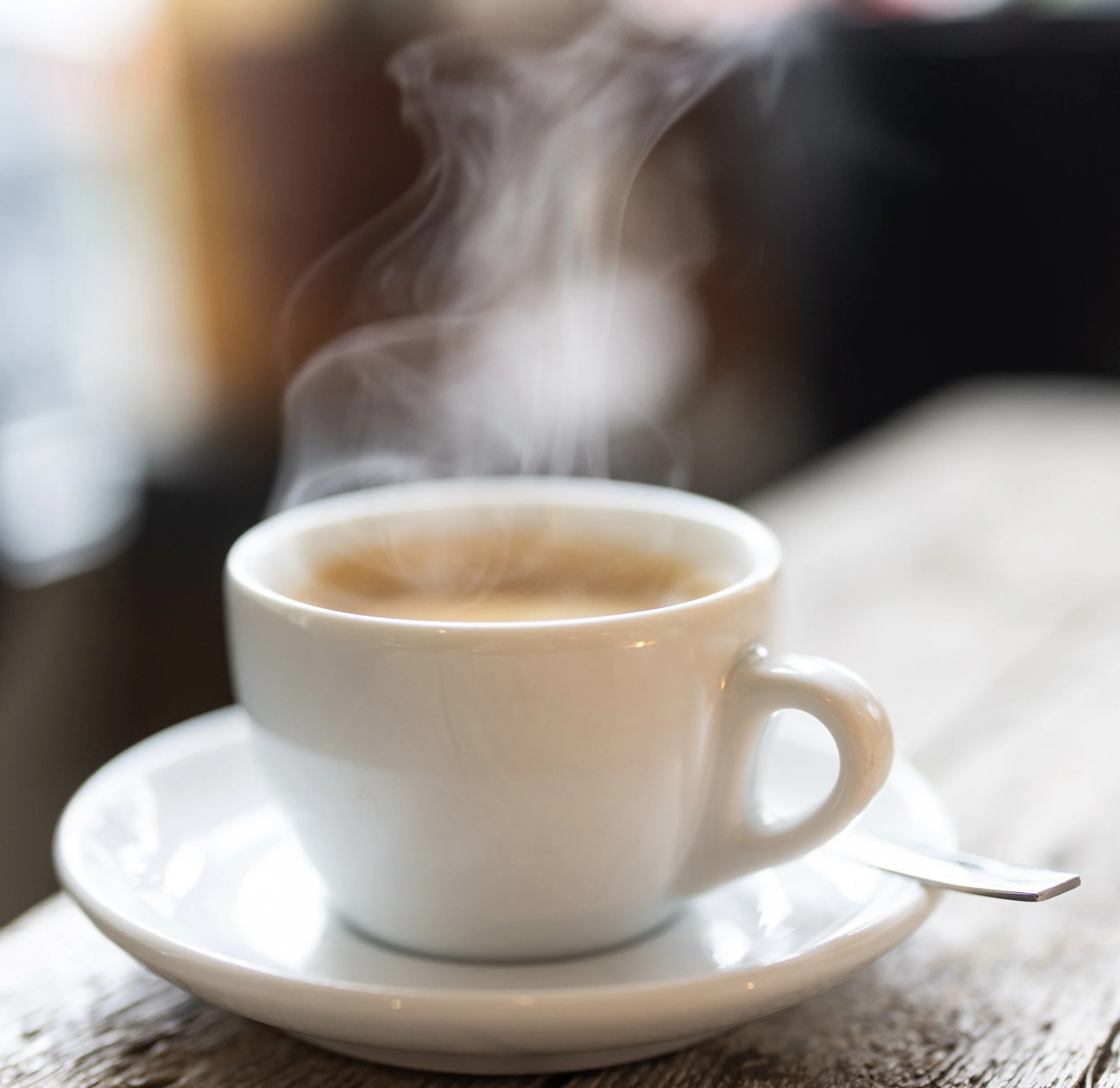Close-up of steam rising from a cup of coffee or tea on a wooden surface.
