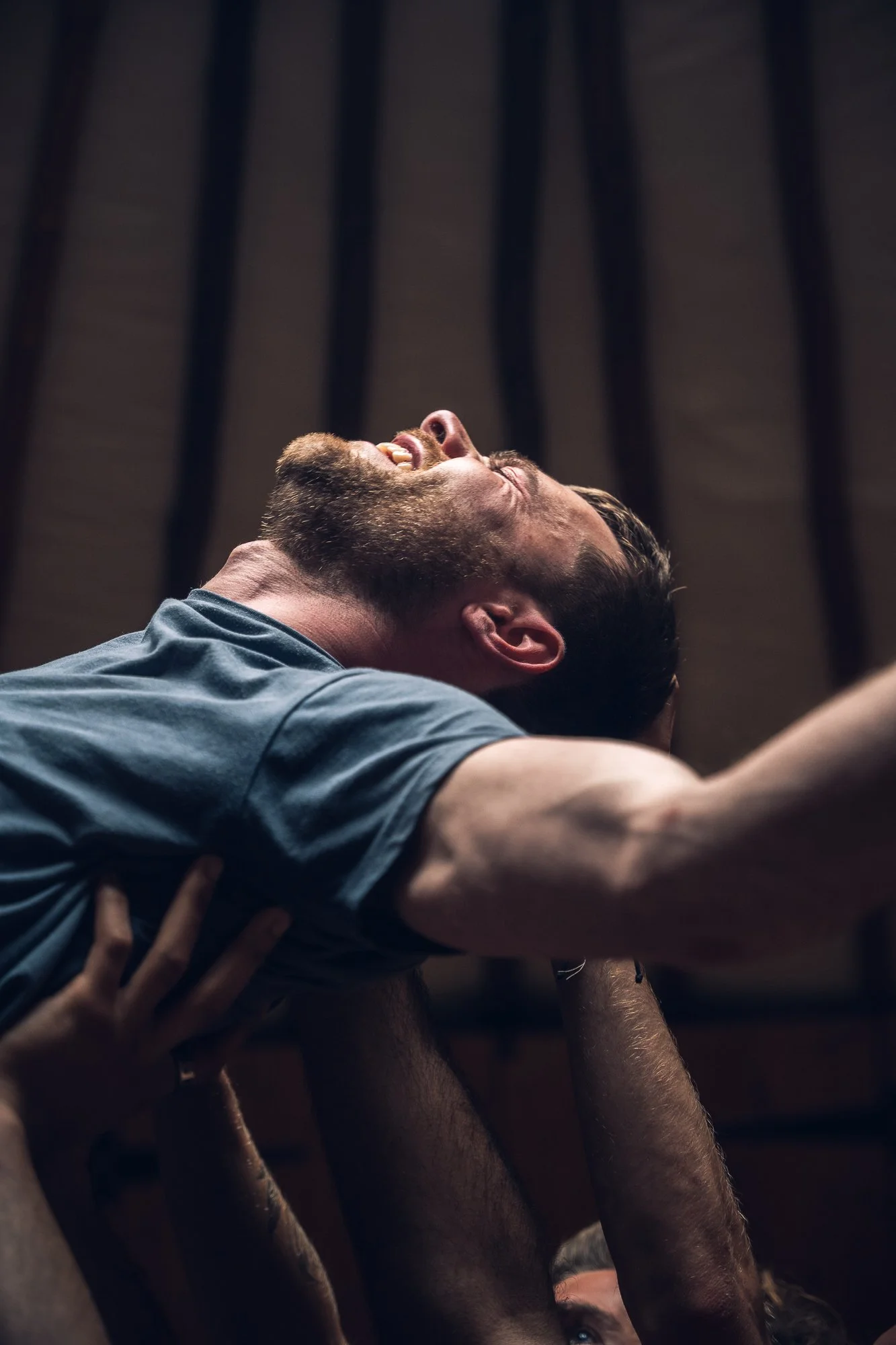 People lifting a man during a celebration or event, with a wooden ceiling in the background.