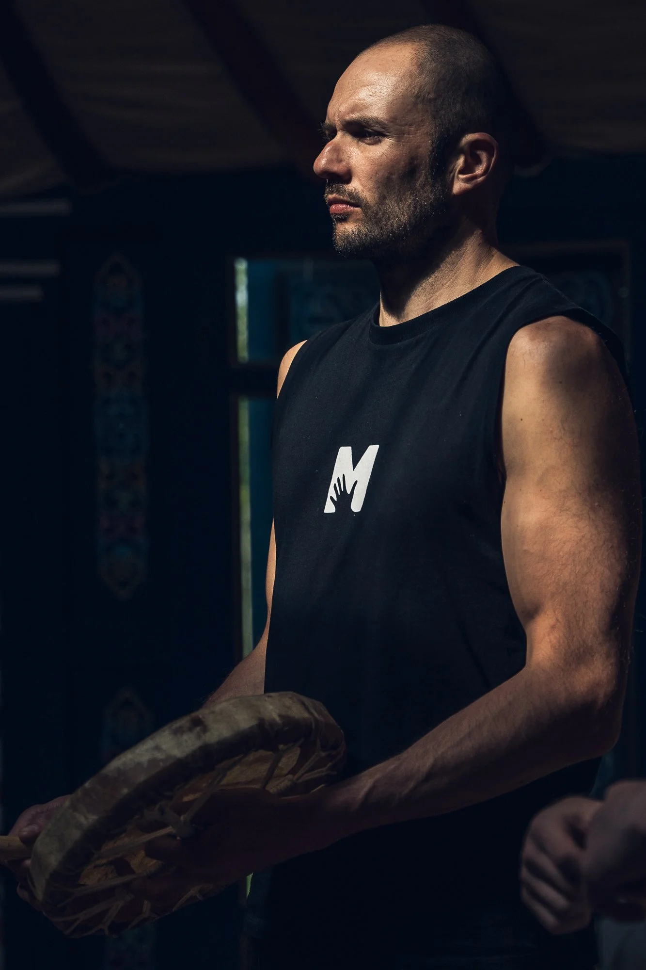 A man with a bald head and beard holding a baseball mitt inside a dimly lit room.