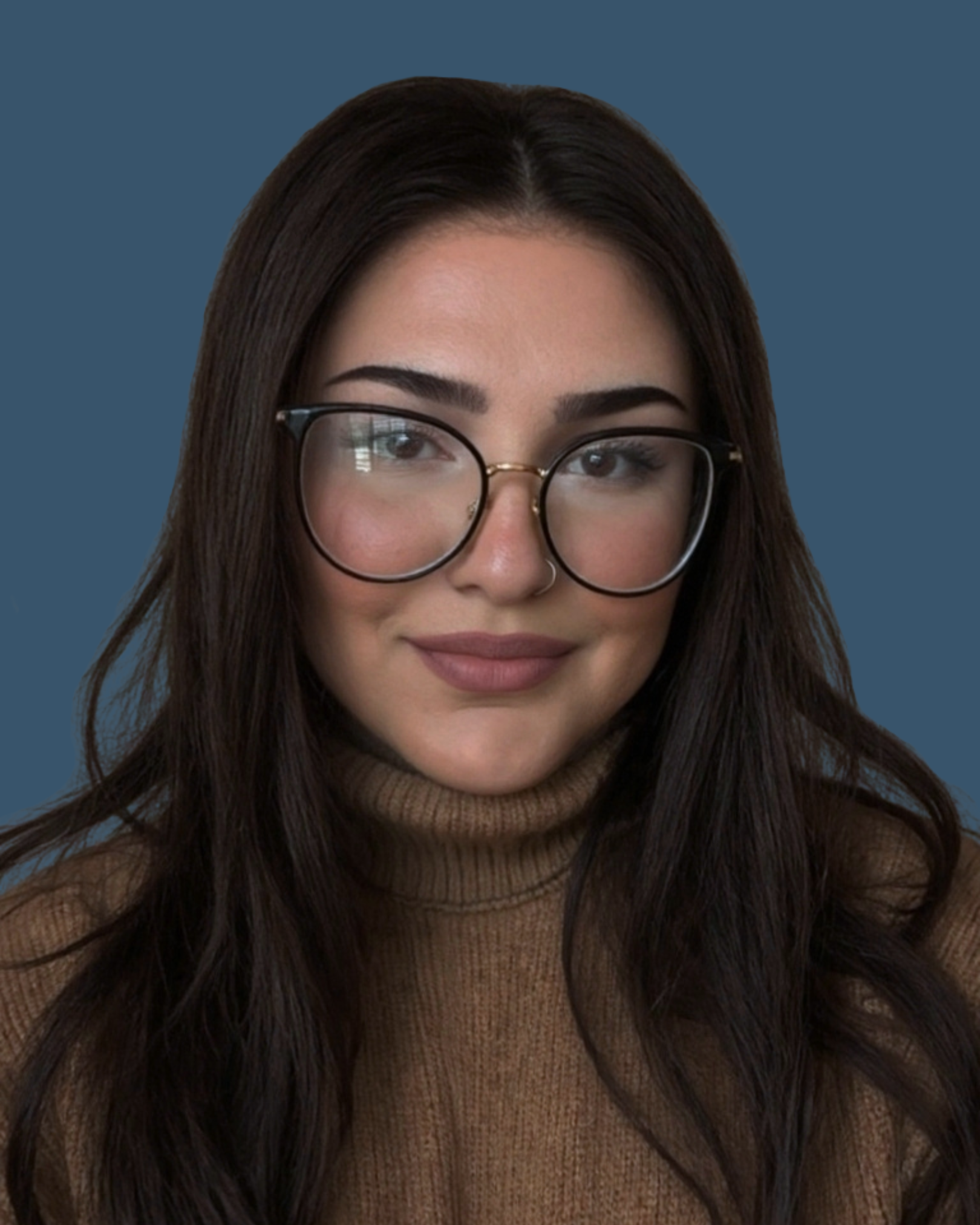 A woman with long dark hair, wearing glasses, a nose ring, and a brown turtleneck sweater, smiling in front of a dark blue background.
