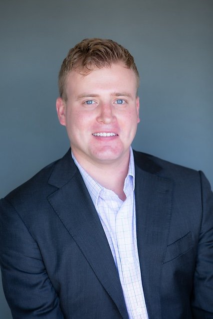 Portrait of Michael DeVris in a suit with a light shirt, smiling against a neutral background.