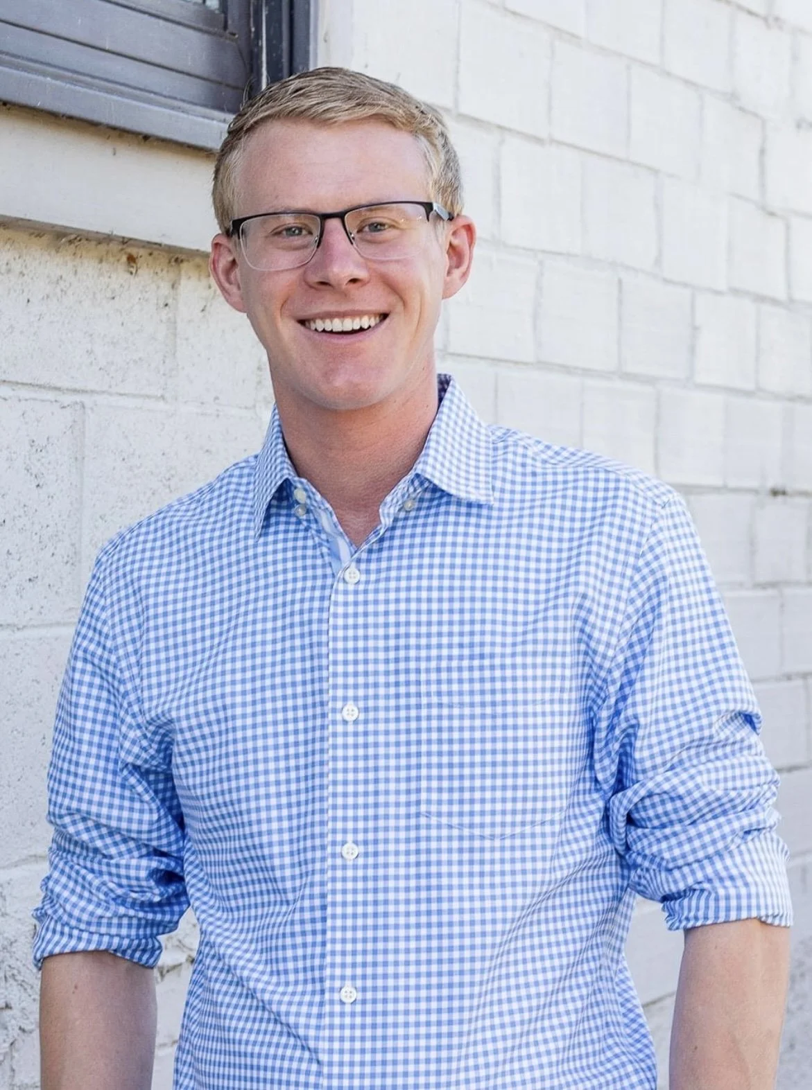 Gerrit DeVris smiling wearing glasses and a blue checkered shirt standing against a brick wall.