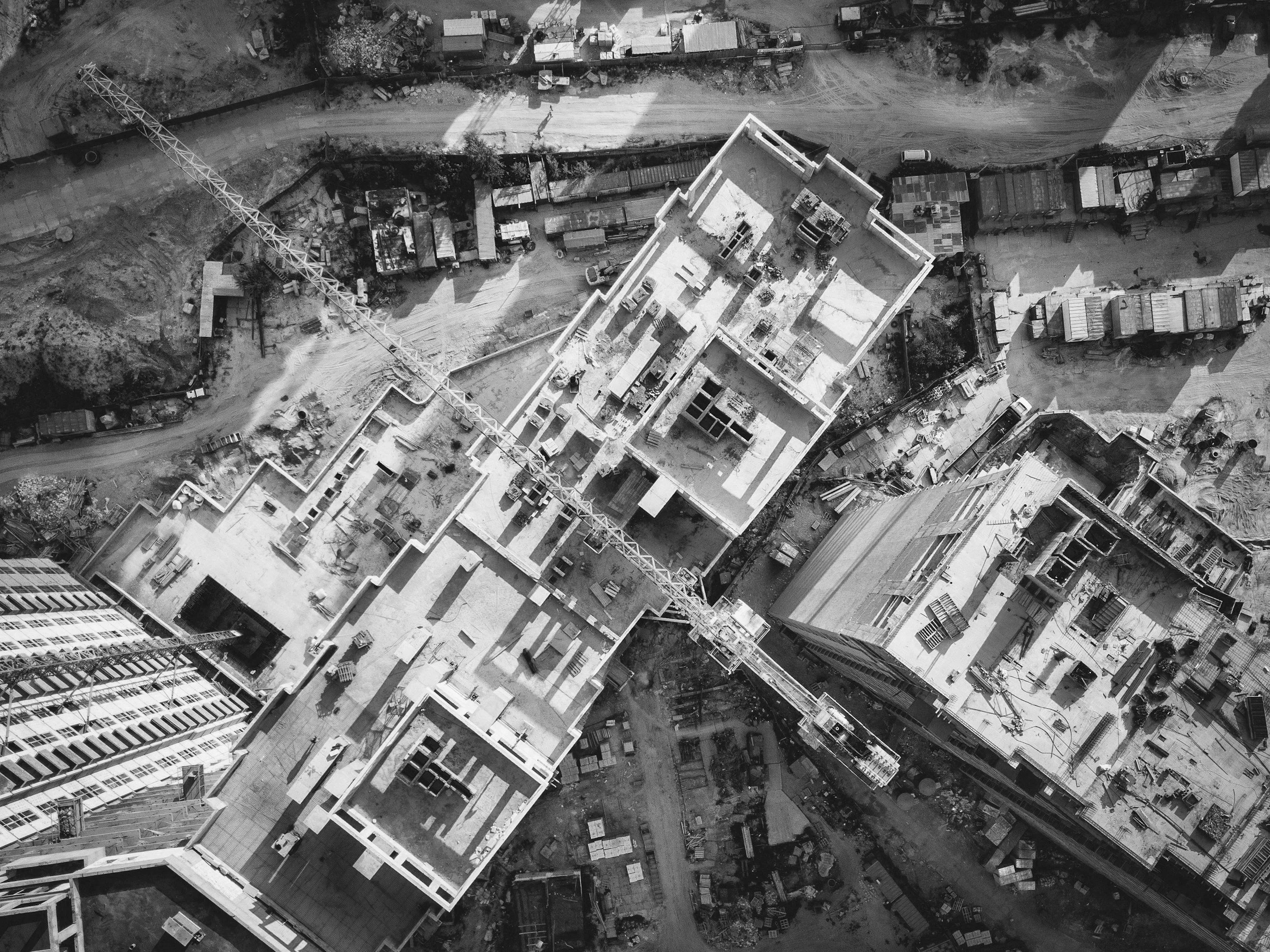 Aerial view of a construction site with multiple buildings under construction, cranes, and scattered building materials.