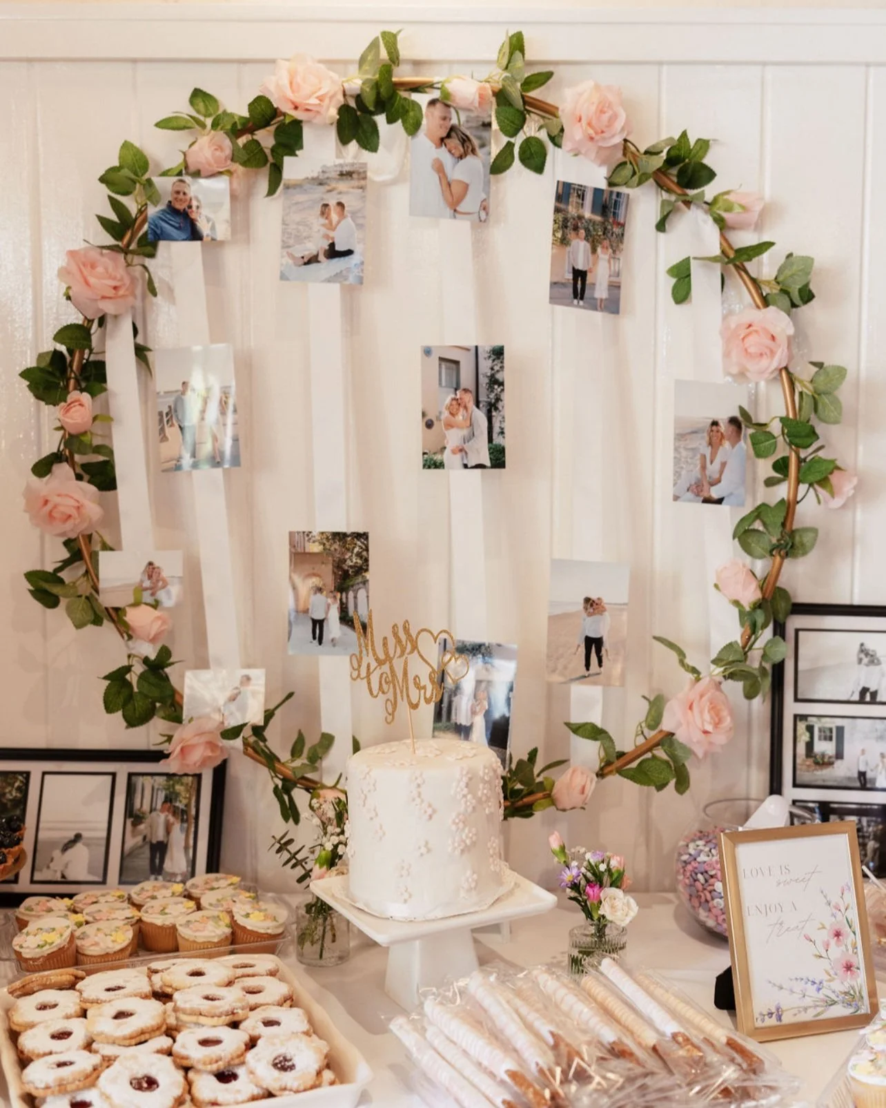 Wedding celebration table with a white cake, cupcakes, cookies, floral decorations, framed photos, and a large heart-shaped photo display with hanging pictures and pink roses. Wedding & Event Planner Hudson Valley, NYC, New York, Bergen County, NJ