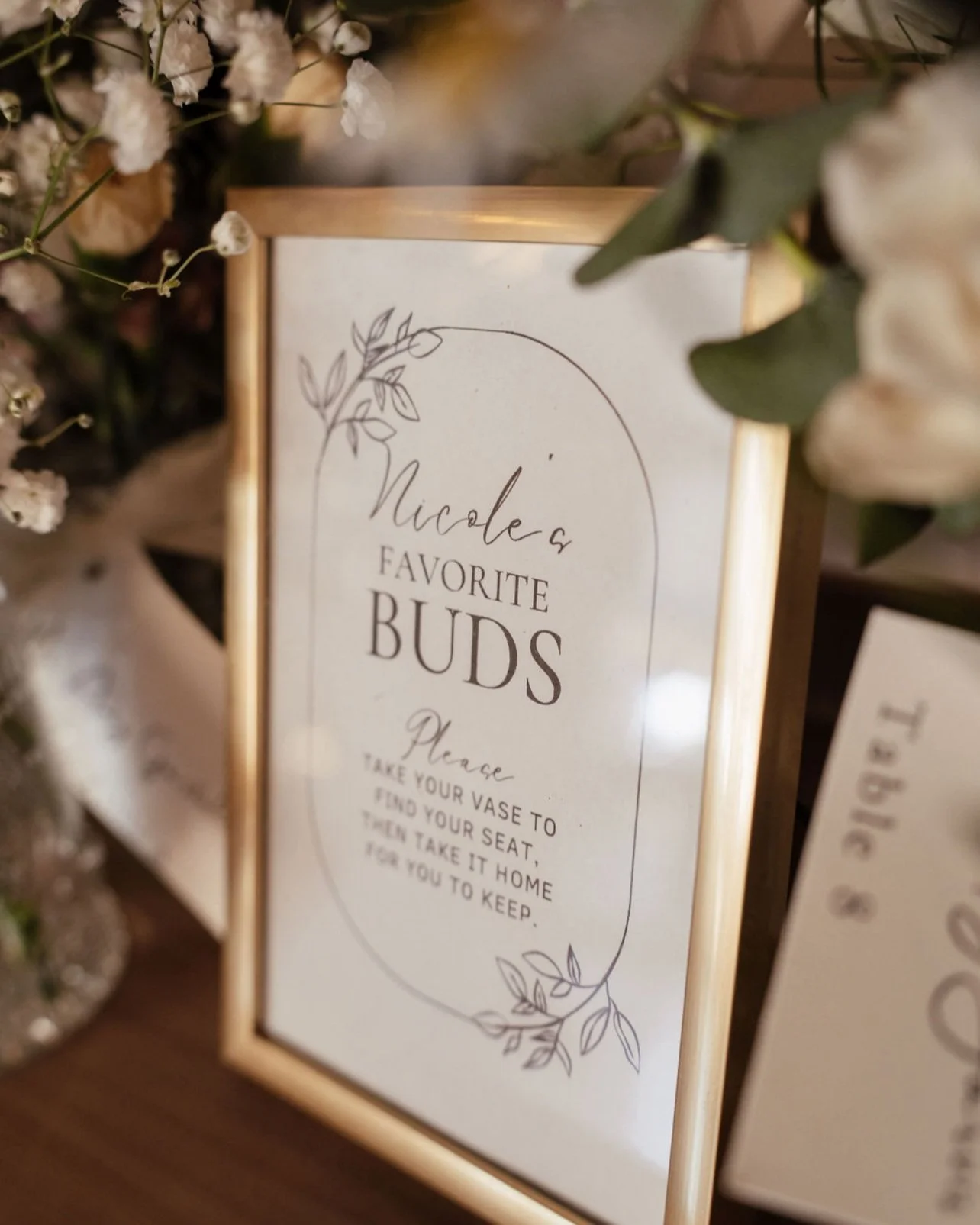 A framed sign titled 'Nicole's Favorite Buds' with floral illustrations, instructing guests to take a vase, find a seat, and take the flowers home to keep. Wedding & Event Planner Hudson Valley, NYC, New York, Bergen County, New Jersey