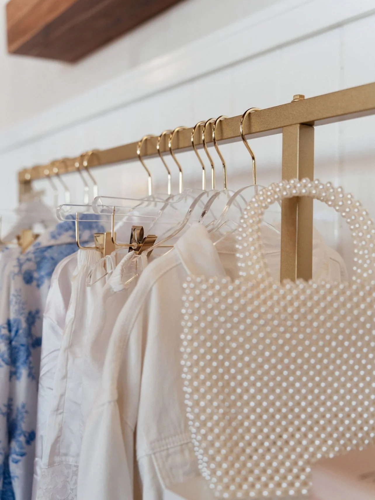 Clothes hanging on a gold rack, including a white blouse, a cream top, and a polka dot dress with pearl embellishments. Wedding & Event Planner Hudson Valley, NYC, New York, Bergen County, New Jersey