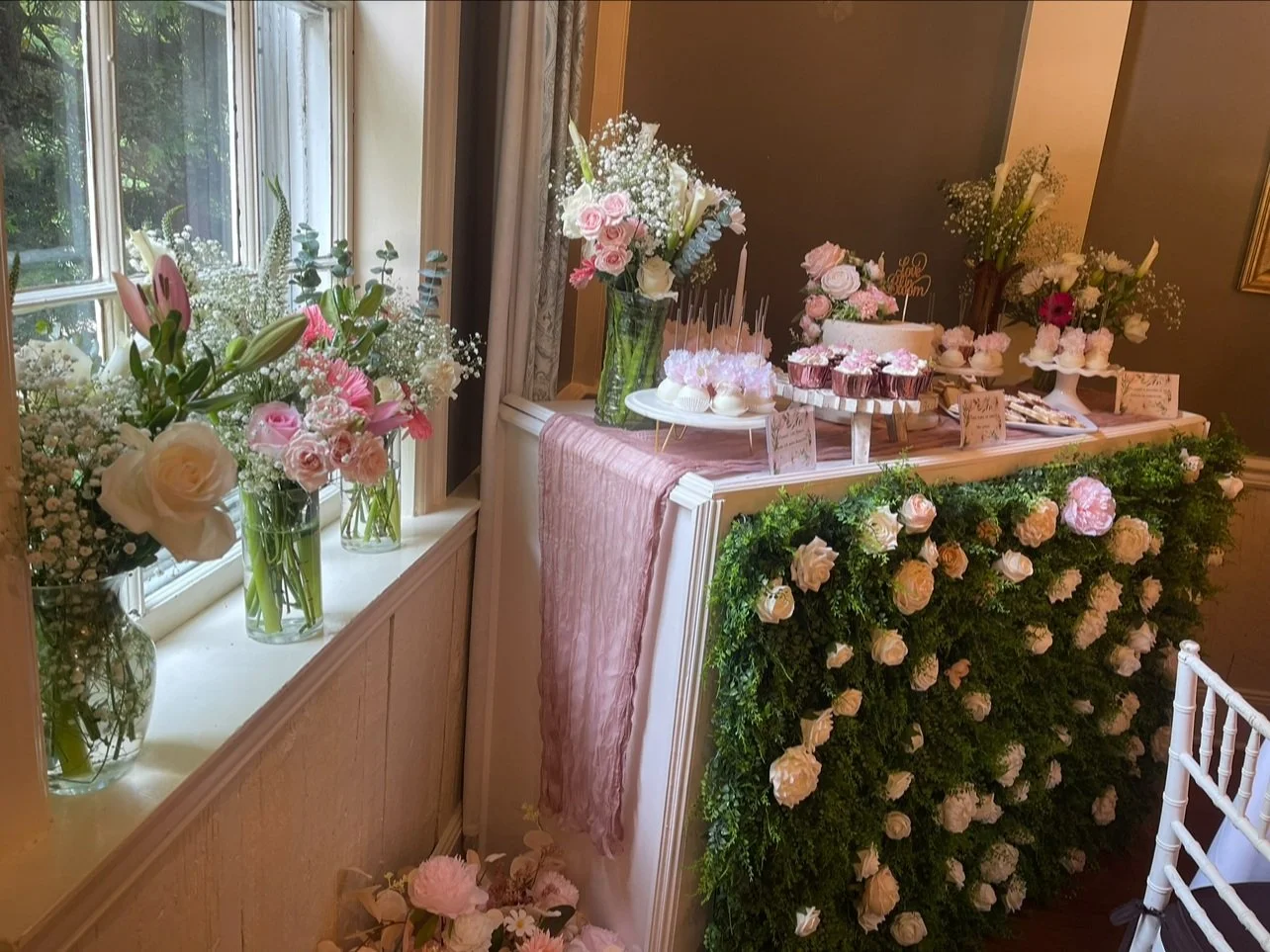 A decorated table at a celebration with pink and white floral arrangements, cupcakes, a cake, and greenery. Wedding & Event Planner Hudson Valley, NYC, New York, Bergen County, New Jersey