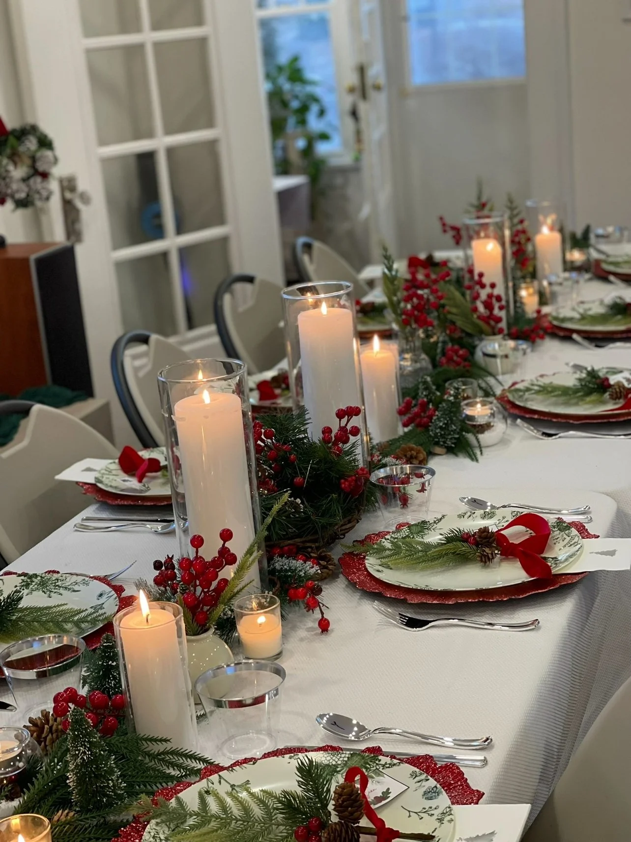 Christmas holiday table setting with candles, pine branches, red berries, and pinecones. Wedding & Event Planner Hudson Valley, NYC, New York, Bergen County, New Jersey