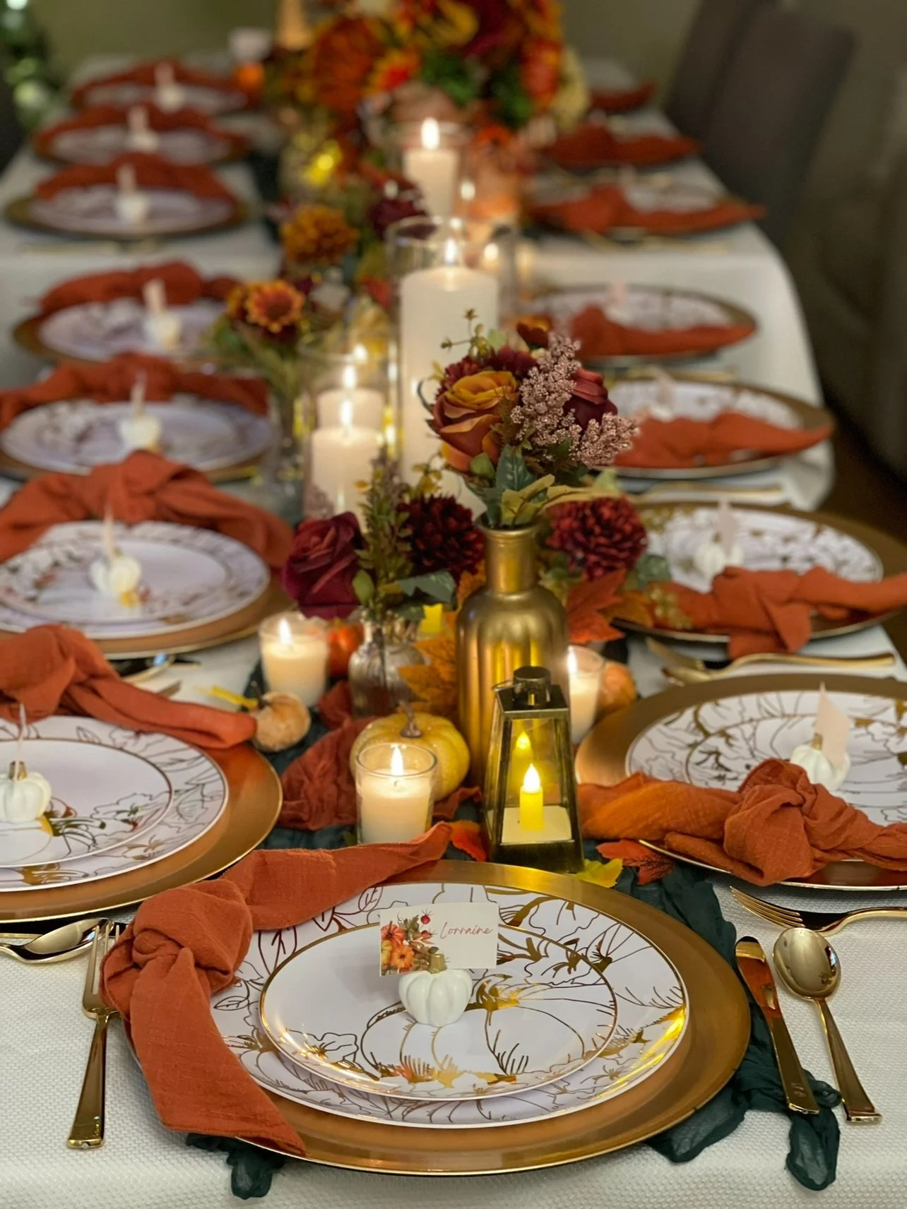 Elegant fall-themed table setting with white and gold plates, orange napkins tied at the side, gold utensils, candles, and floral centerpieces with orange, burgundy, and green autumn flowers. Wedding & Event Planner Hudson Valley, NYC, New York, NJ