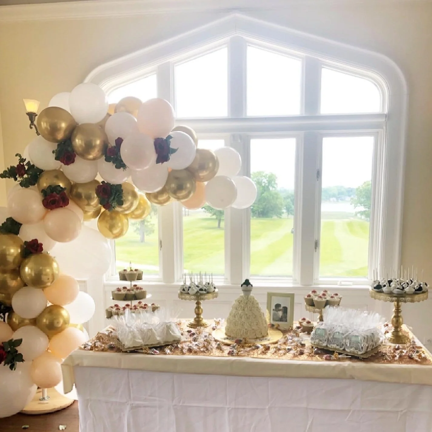Party table with a cake, cupcakes, and treats, decorated with balloon garlands and floral accents, set in front of large window views of green fields. Wedding & Event Planner Hudson Valley, NYC, New York, Bergen County, New Jersey