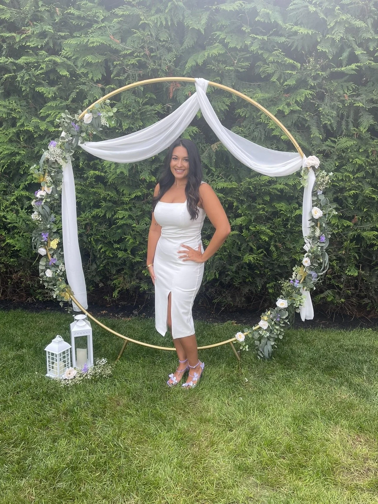 A woman in a white dress standing outdoors on grass with a decorative floral and fabric circle backdrop. Wedding & Event Planner Hudson Valley, NYC, New York, Bergen County, New Jersey