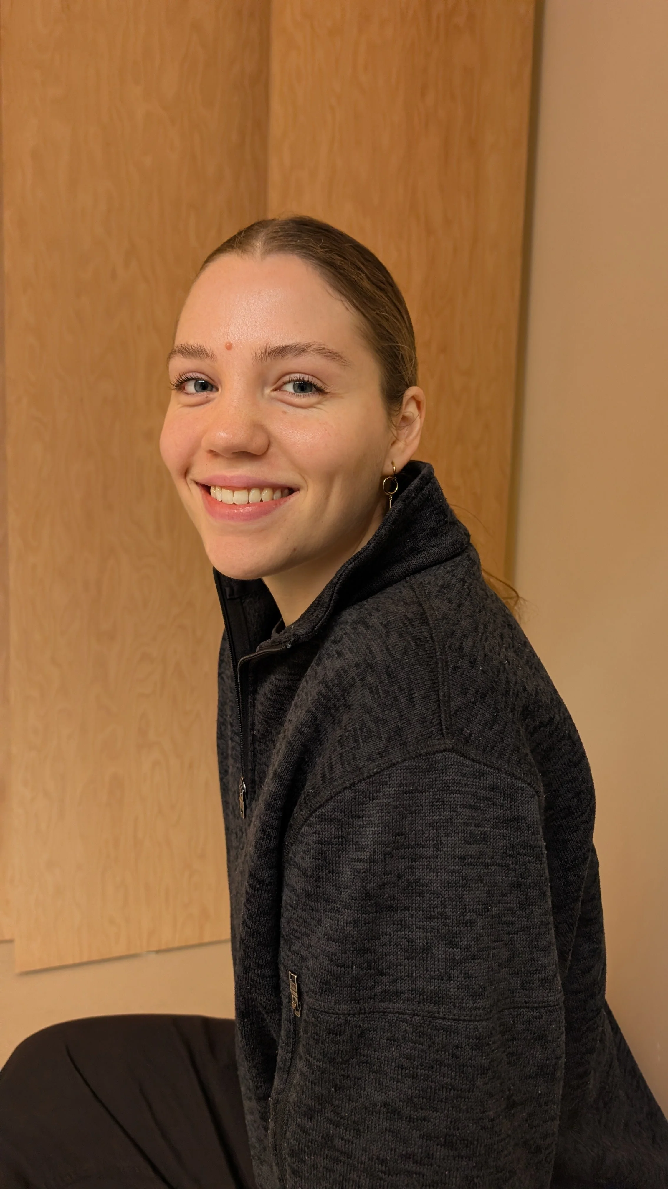 Smiling woman in blue athletic wear holding a black yoga circle around her head.