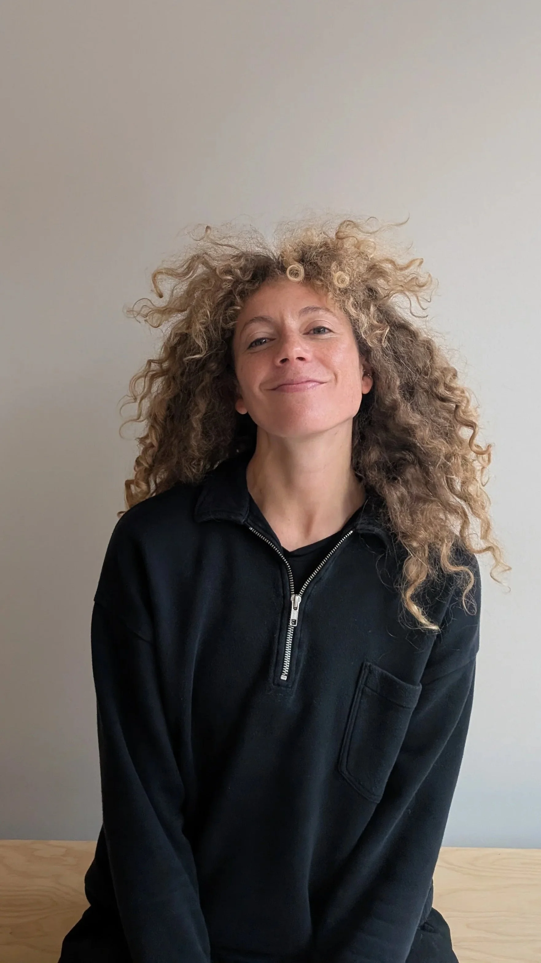 Close-up of a smiling woman with glasses and hoop earrings, wearing a striped shirt, in an indoor setting.
