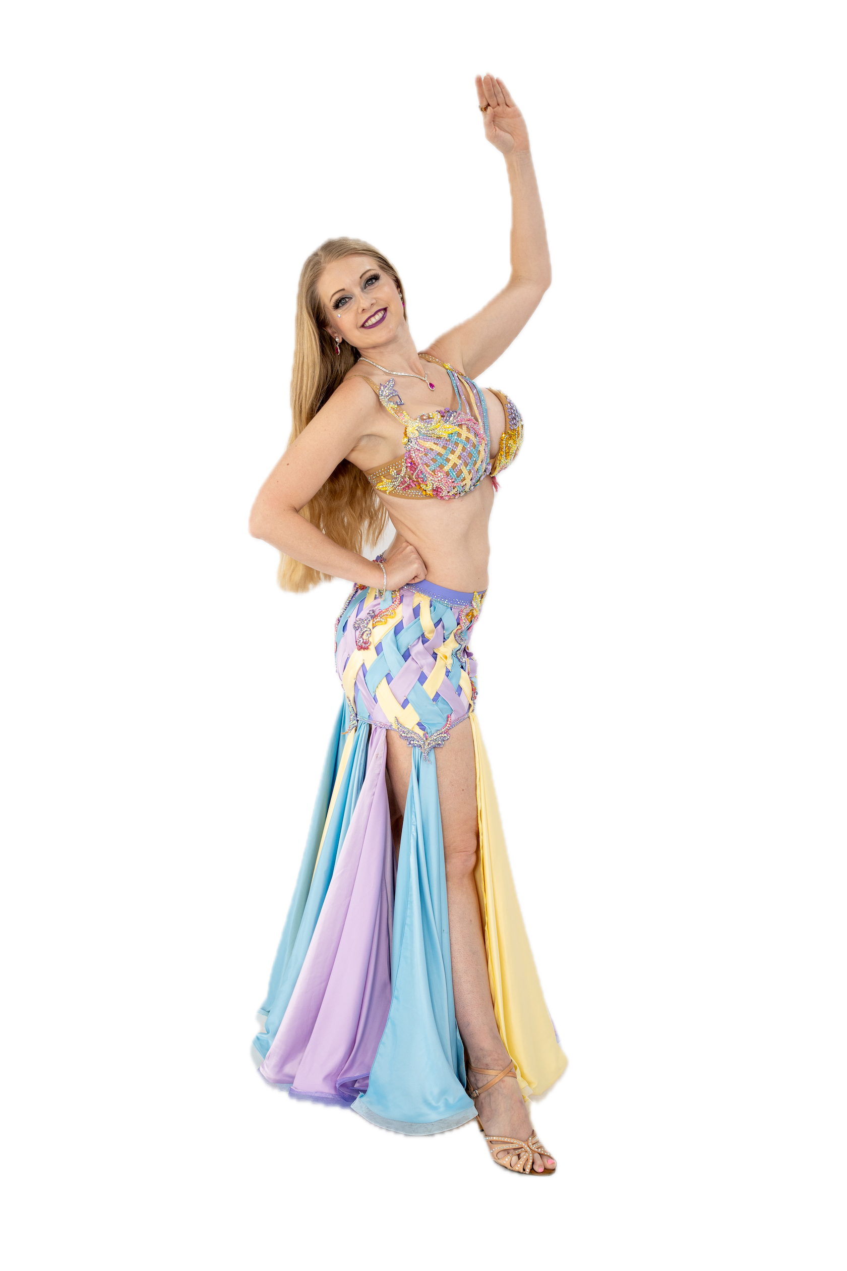 Woman wearing a colorful, intricately designed belly dance costume, raising one hand, smiling, with long hair and high heel shoes.