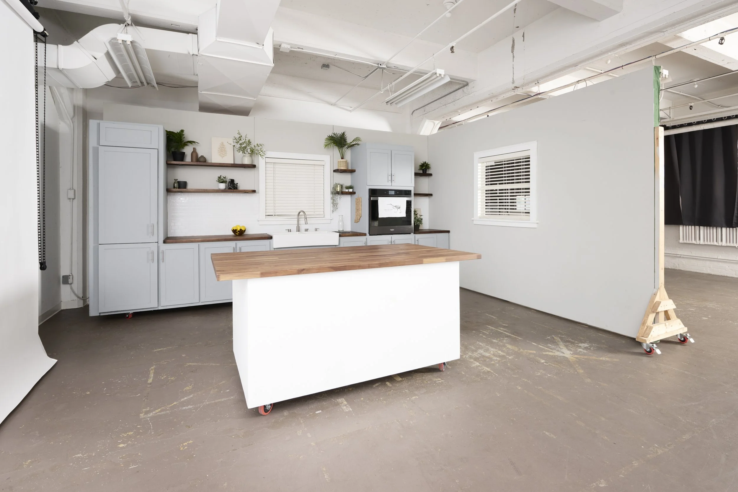 Kitchen set with island, and mobile wall with curtains drawn on East window wall behind