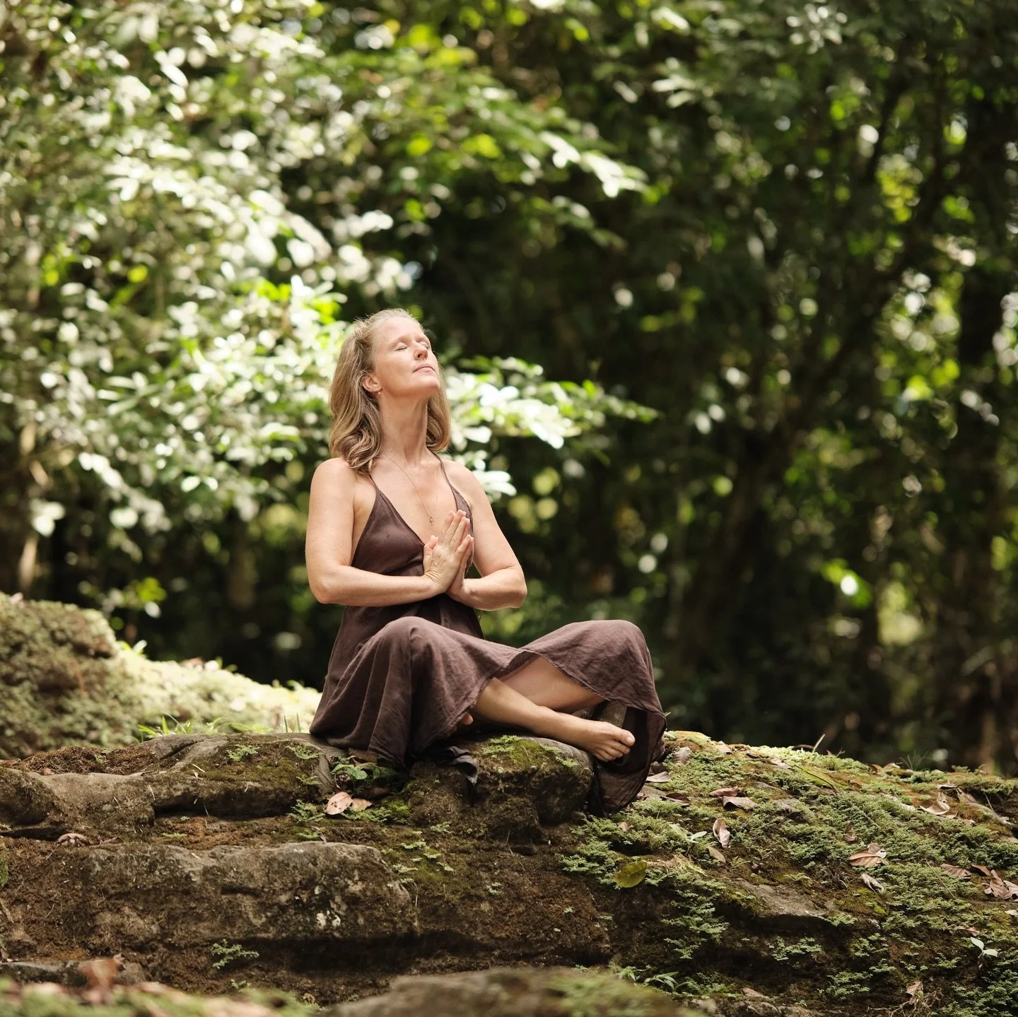 A slow sequence of stillness: meditating with the current beneath, hands held like a quiet prayer as she lifts her face to the sky, then subtle, dance‑like movements through soft, even light, and finally a backlit frame from the forest&rsquo;s leafy 