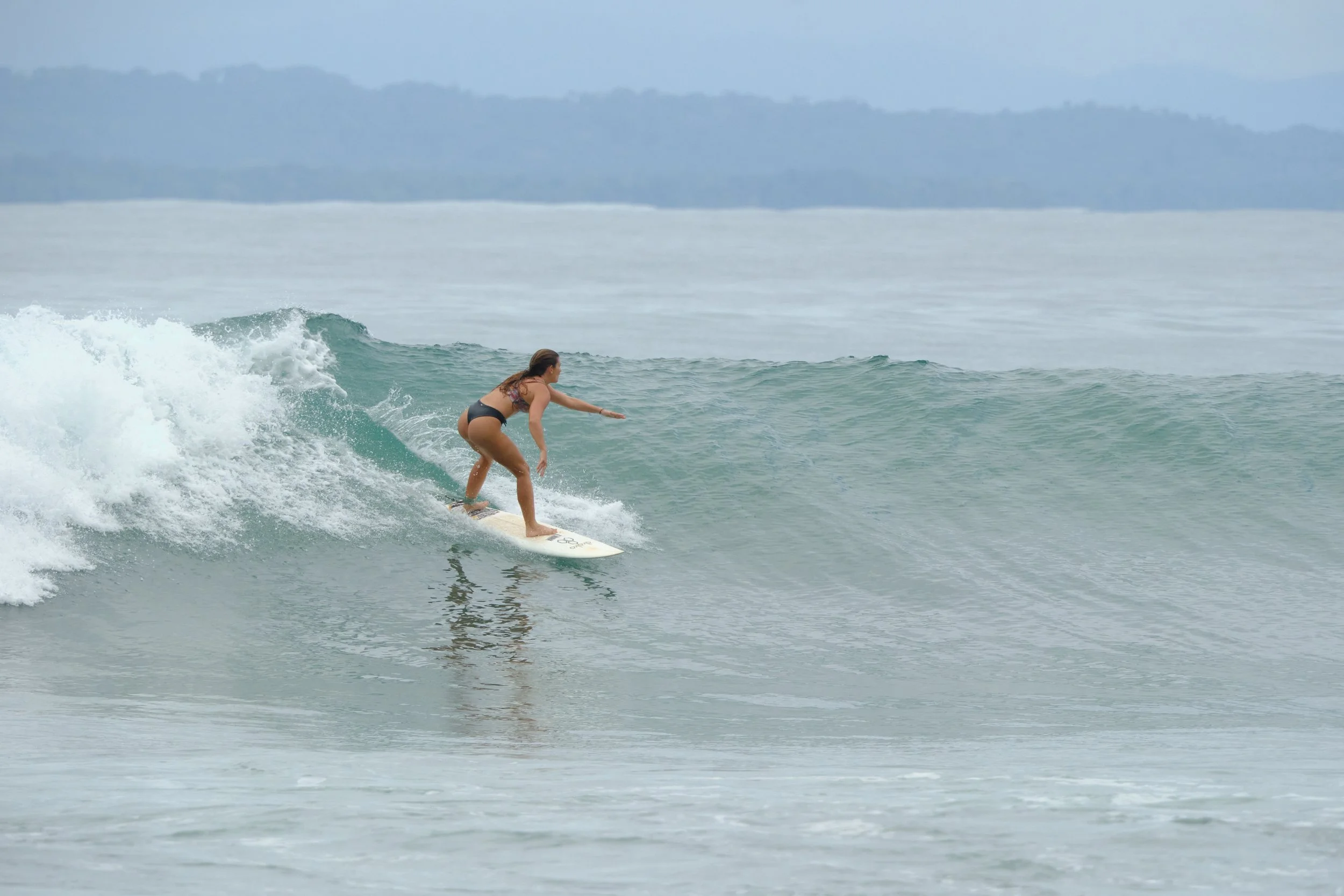 A woman surfing on a wave in the ocean during daytime, wearing a bikini.
