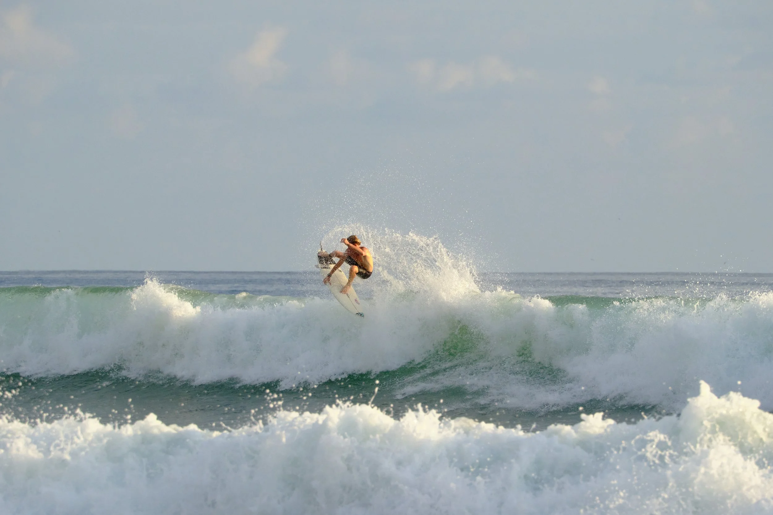 A person surfing on a wave in the ocean under a partly cloudy sky.
