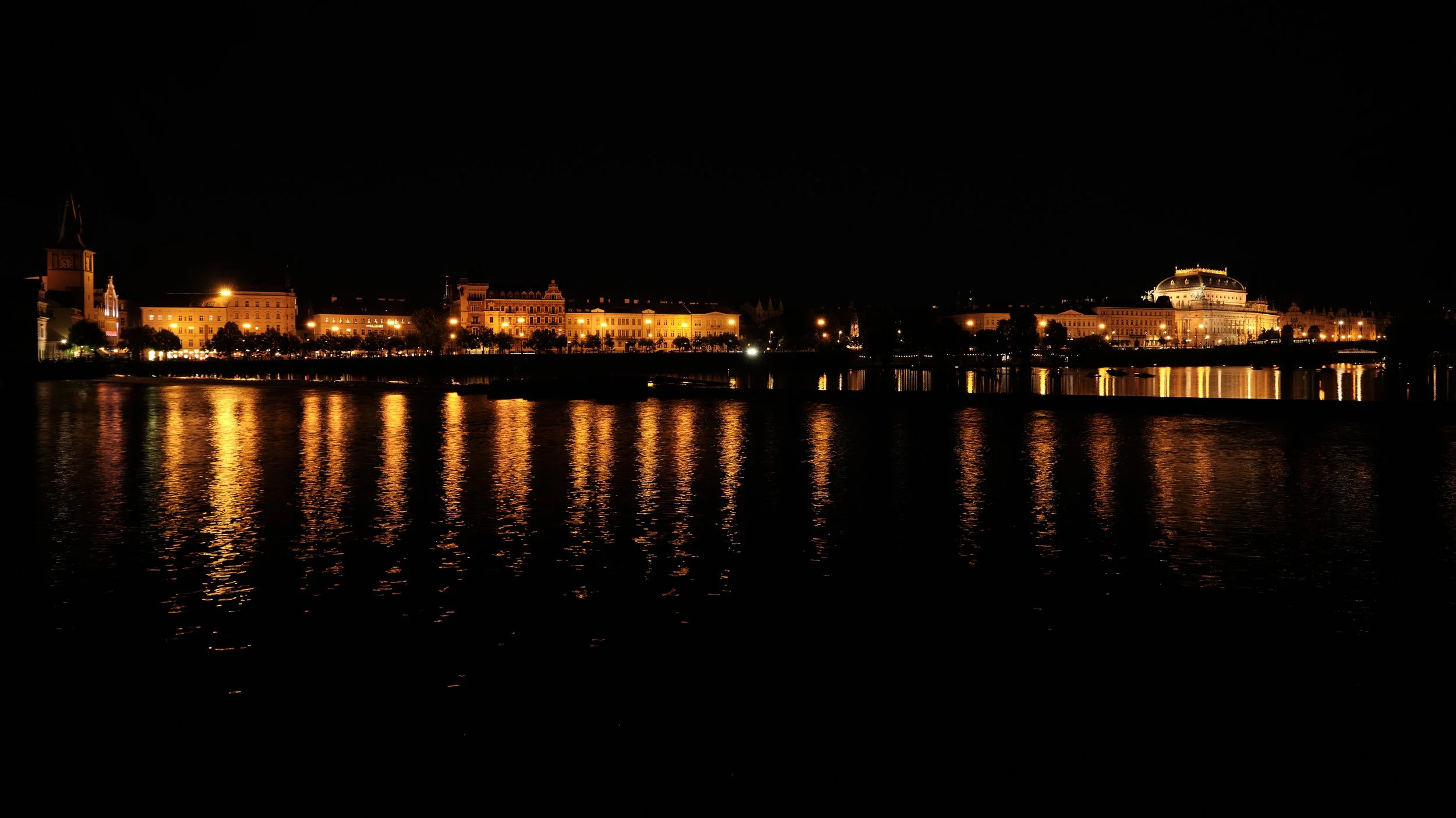Historic landmarks glow along the Vltava River, their reflections dancing across the water and revealing a city that feels just as timeless beneath the night sky.