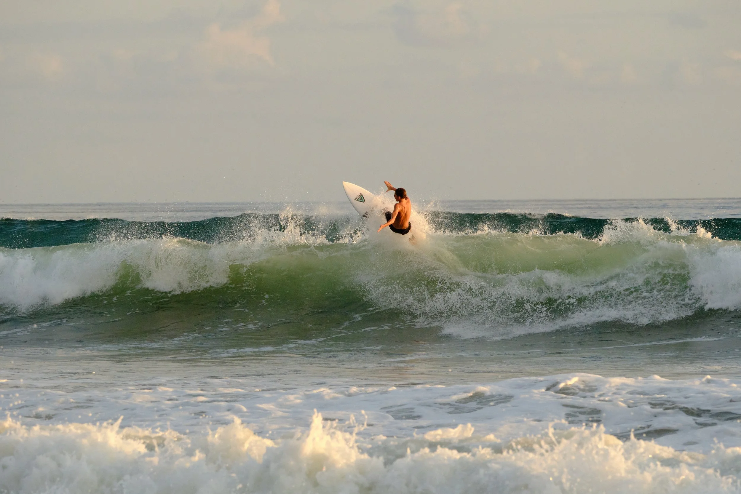 A man surfing on a wave in the ocean during what appears to be late afternoon or early evening.
