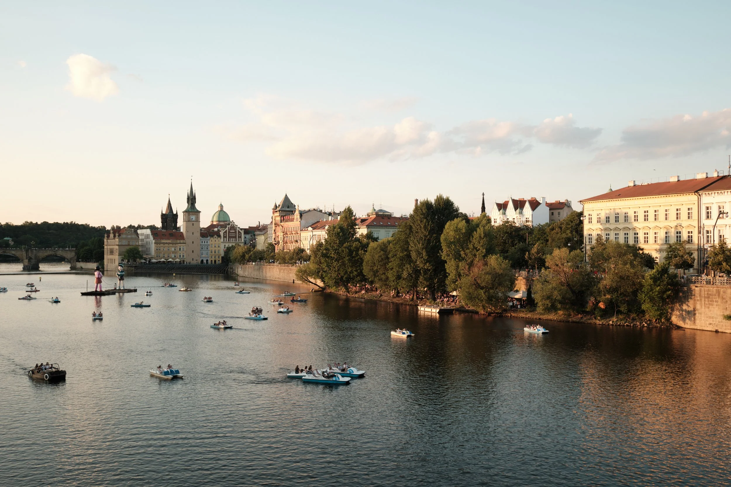 As the afternoon light softens over the Vltava River, Prague settles into one of its favorite summer rituals. Paddle boats drift across the water while the city’s historic skyline glows in warm tones, blending centuries of history with the simple joy