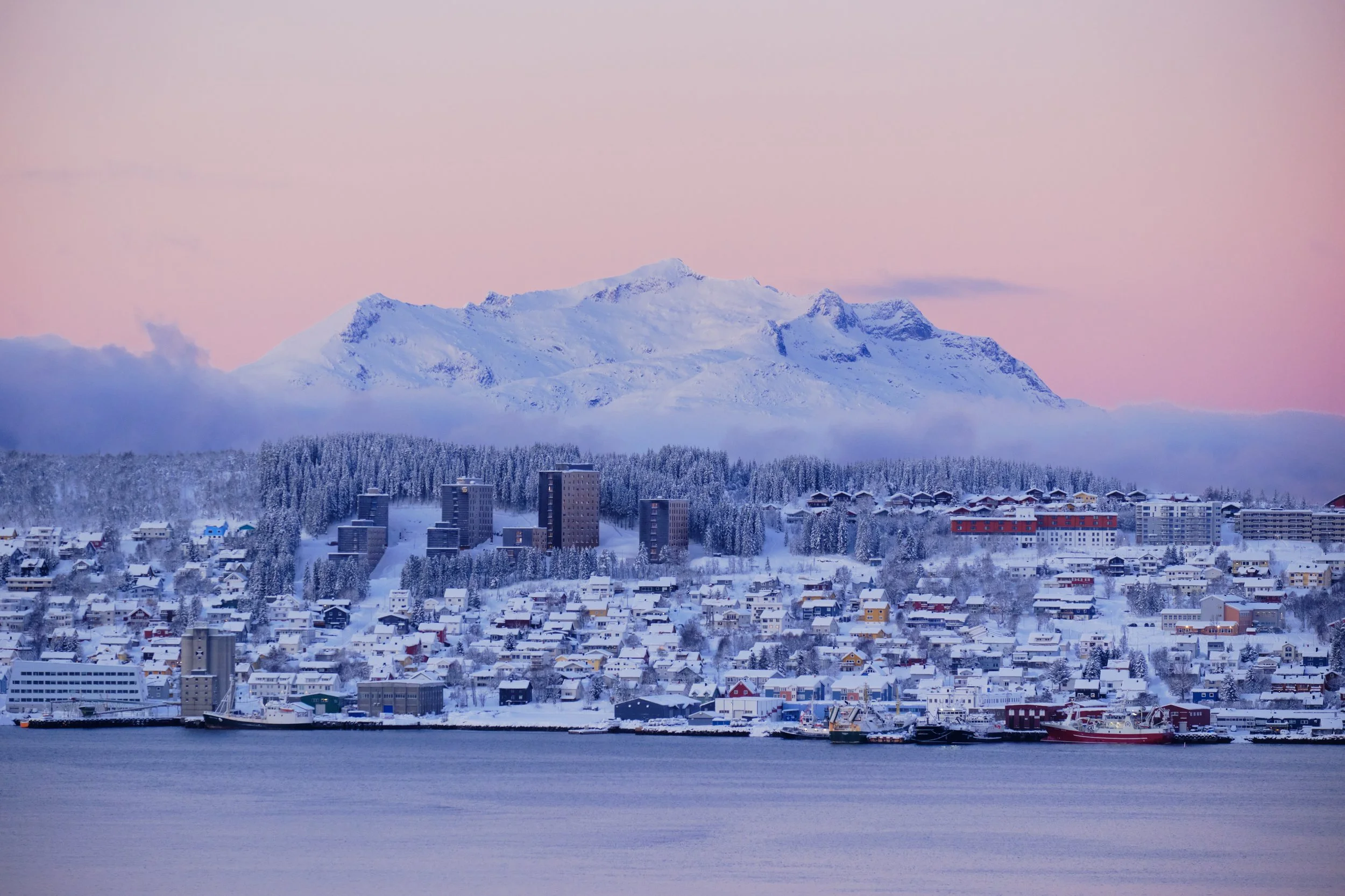 As daylight gradually strengthened, Tromsø revealed another side of itself. Snow-covered mountains rose quietly beyond the city, while pastel shades of pink and blue settled across the Arctic sky. Every rooftop, shoreline, and distant peak seemed wra