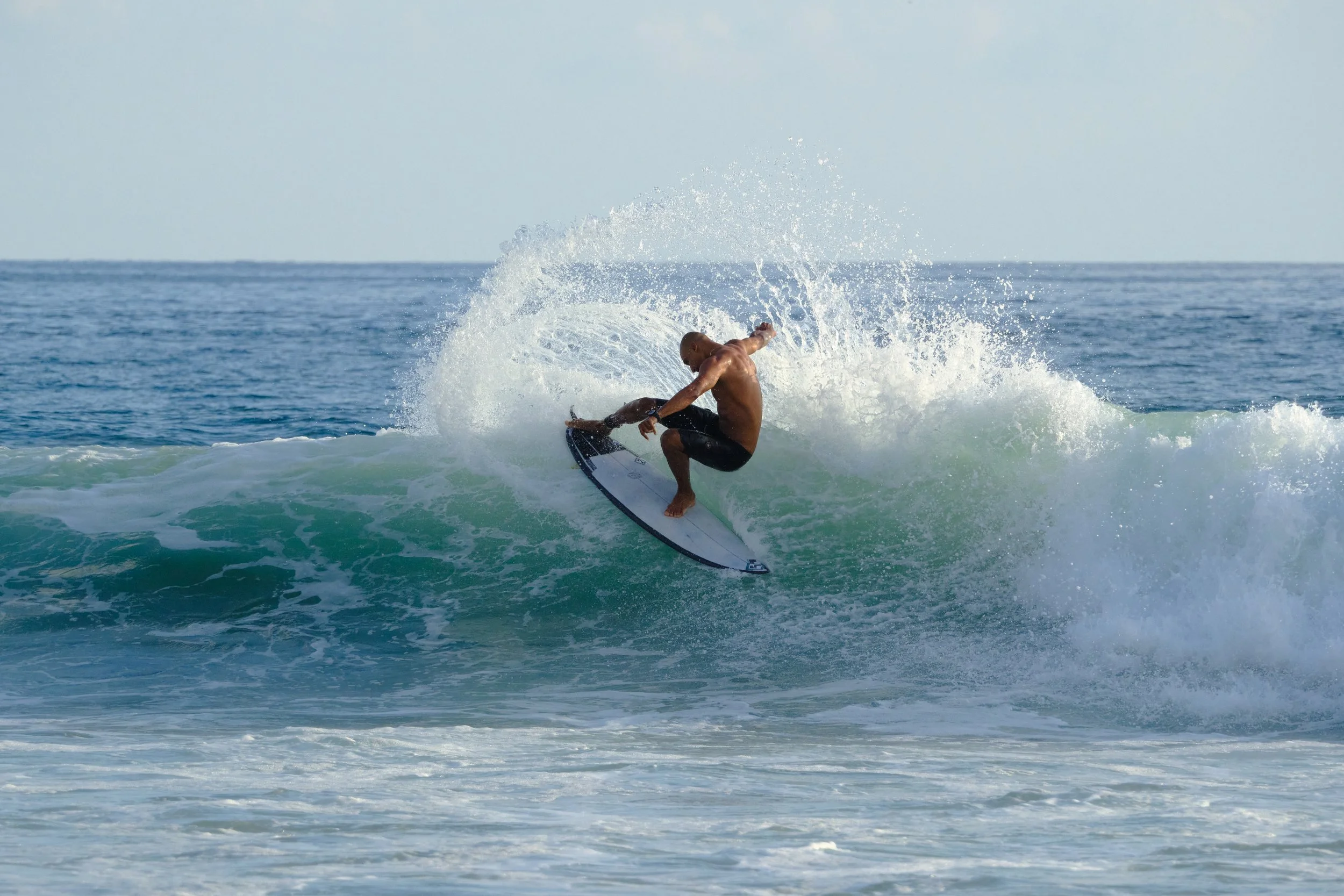 A male surfer riding a wave at the beach on a sunny day.