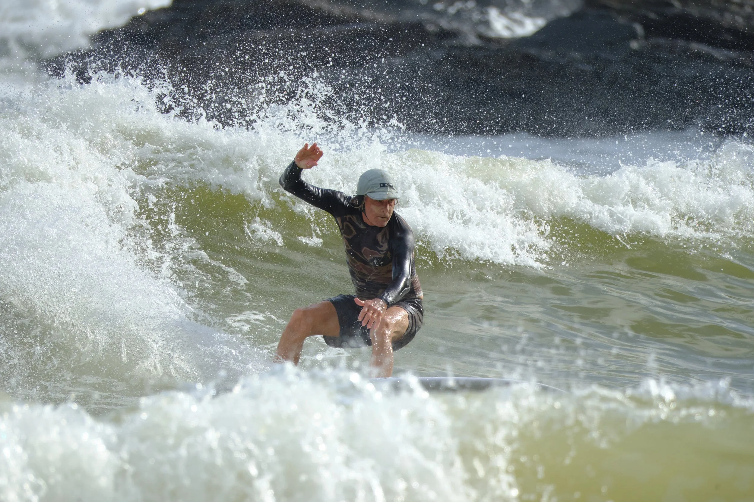 A person wearing a hat surfing on a wave in the ocean.
