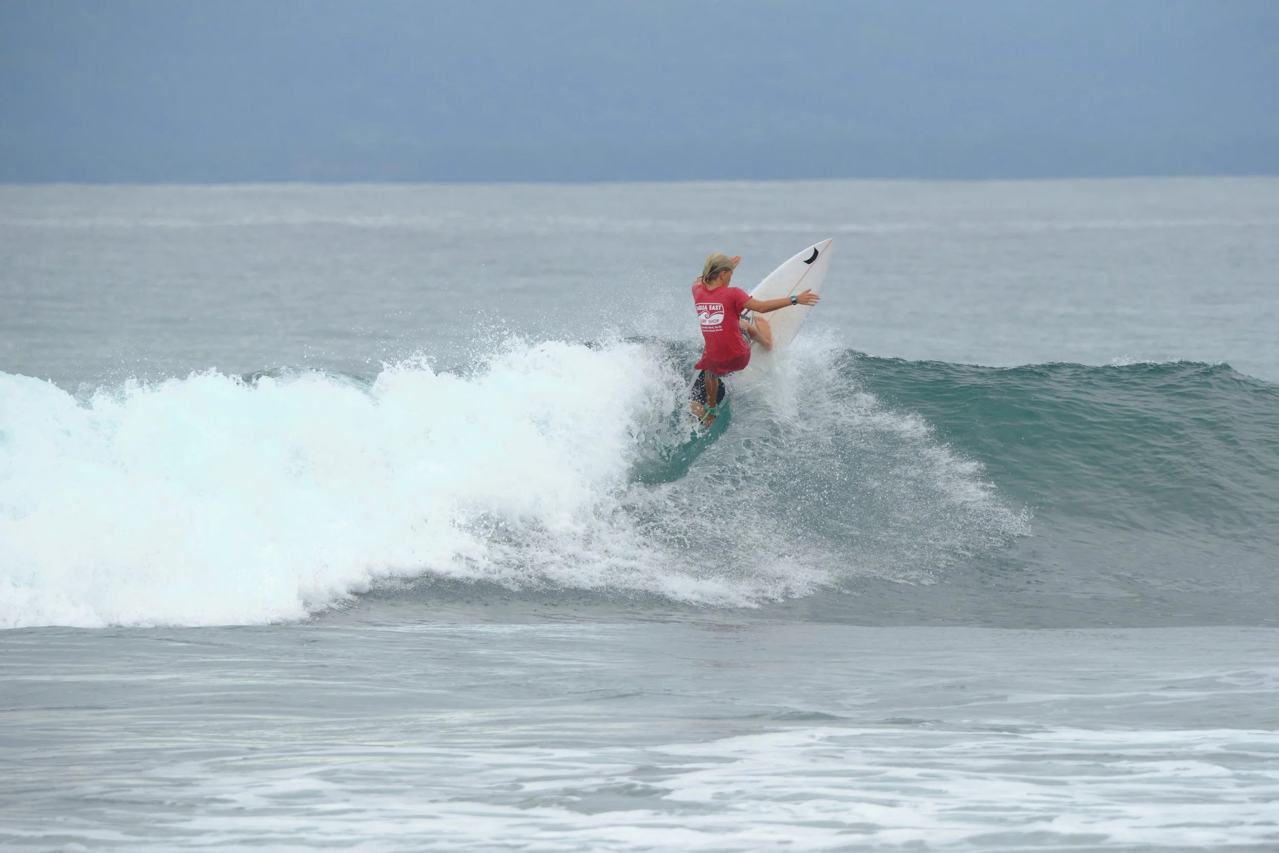 A surfer riding a wave on the ocean with a cloudy sky overhead.