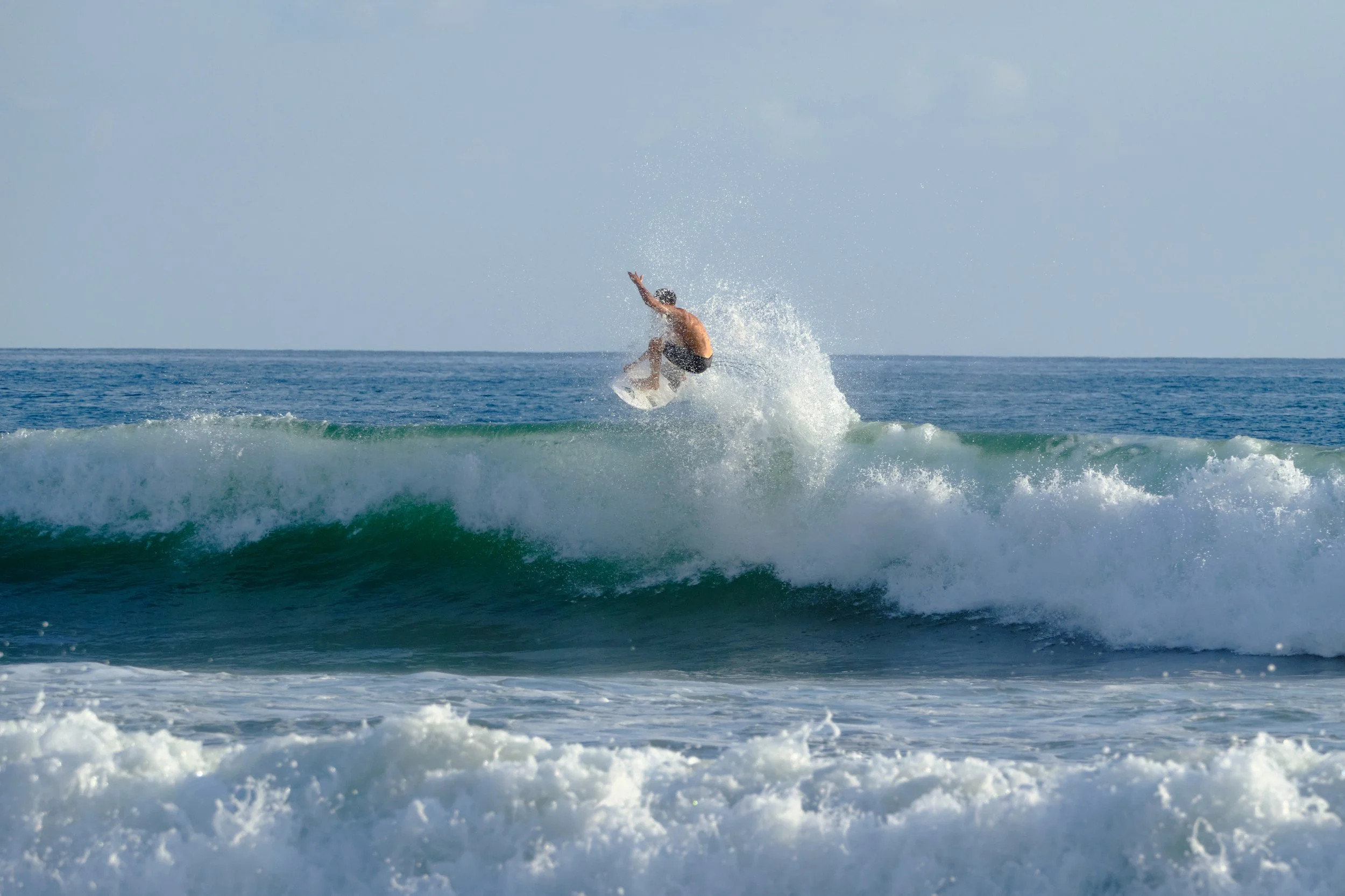 A person surfing on a wave in the ocean, mid-air jump.