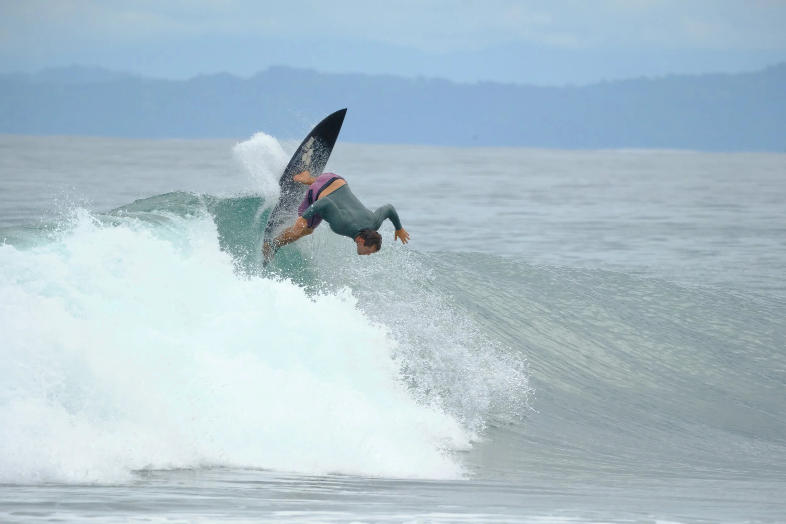 A person falling off a surfboard while riding a wave in the ocean, with distant mountain or island in the background.
